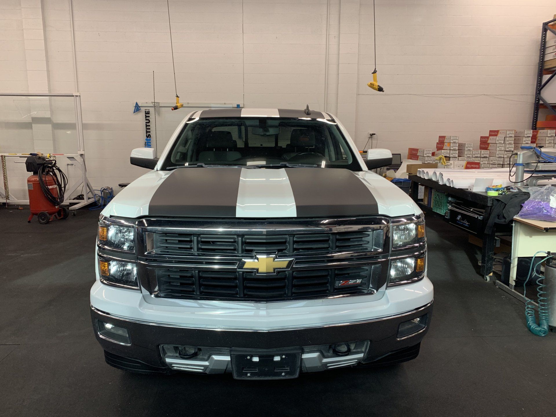 Front view of a black Chevrolet pickup with white racing stripes inside a garage
