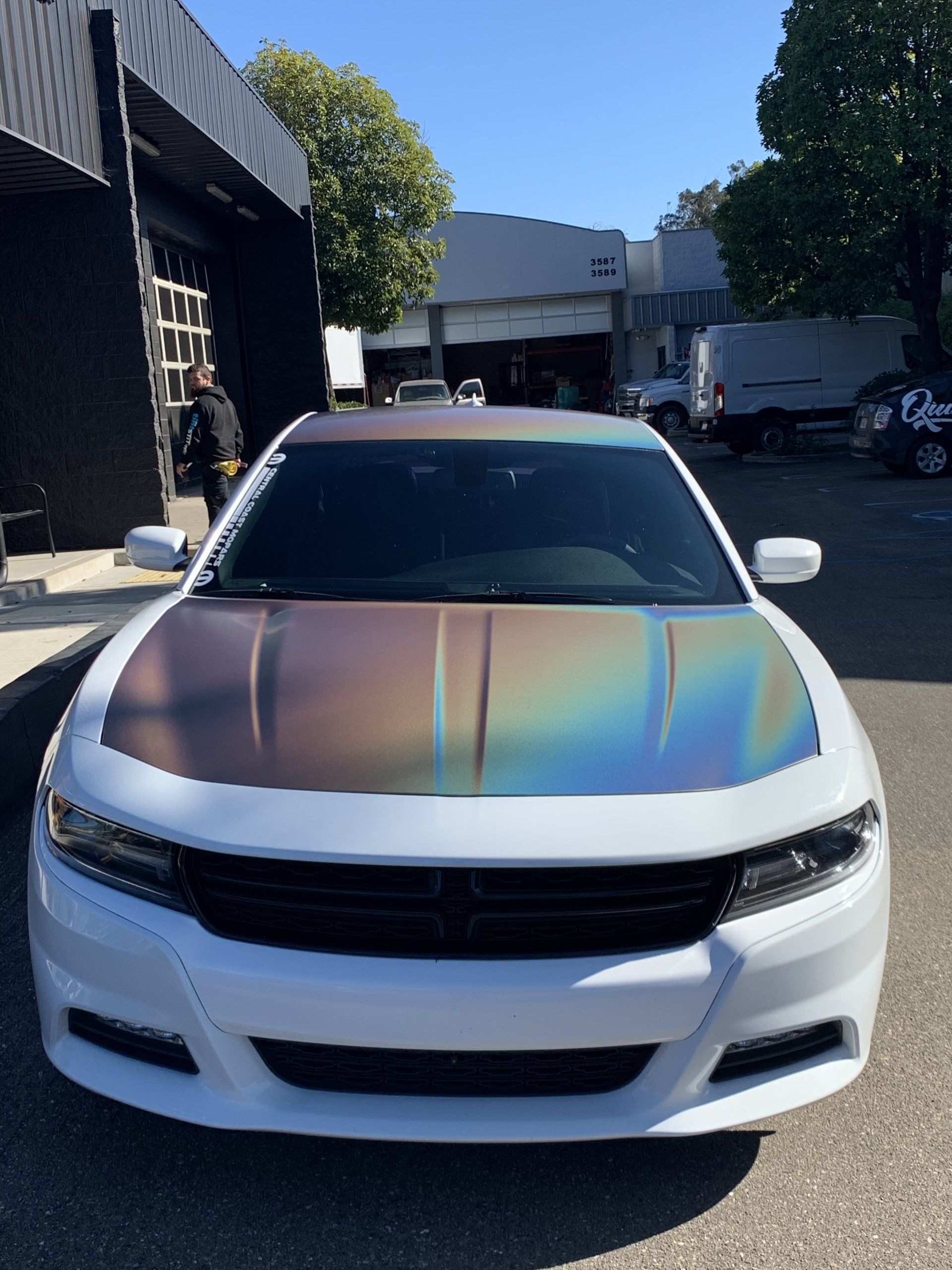 White sedan with a rainbow-colored hood wrap parked outdoors in a lot.