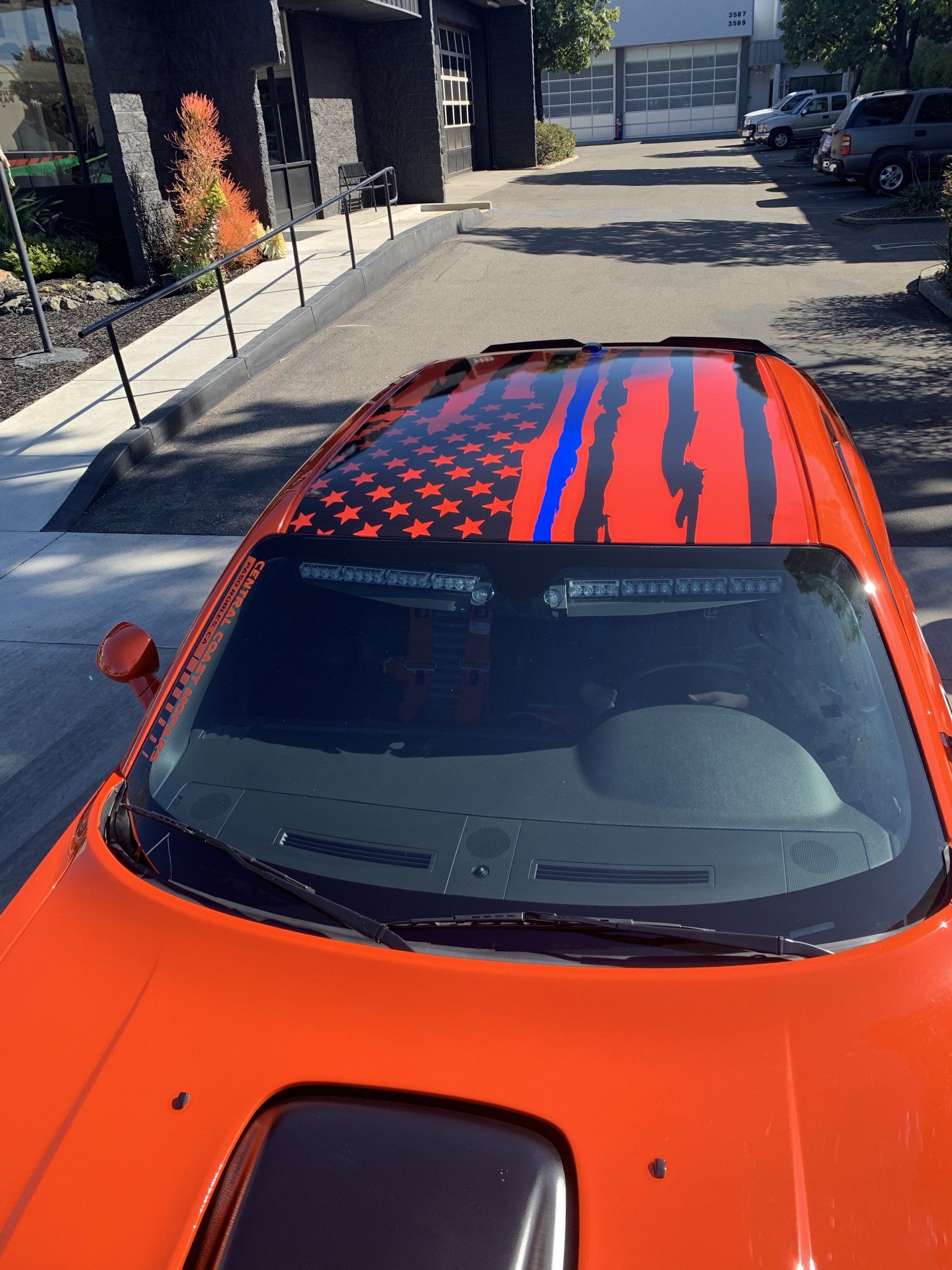 Orange car with red-and-blue striped roof parked on a sunny street