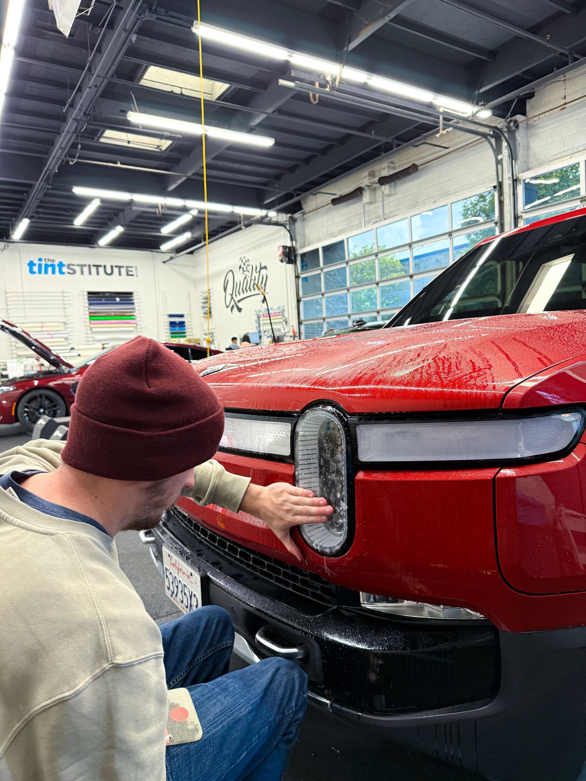 Person polishing the front grille of a red SUV in a workshop
