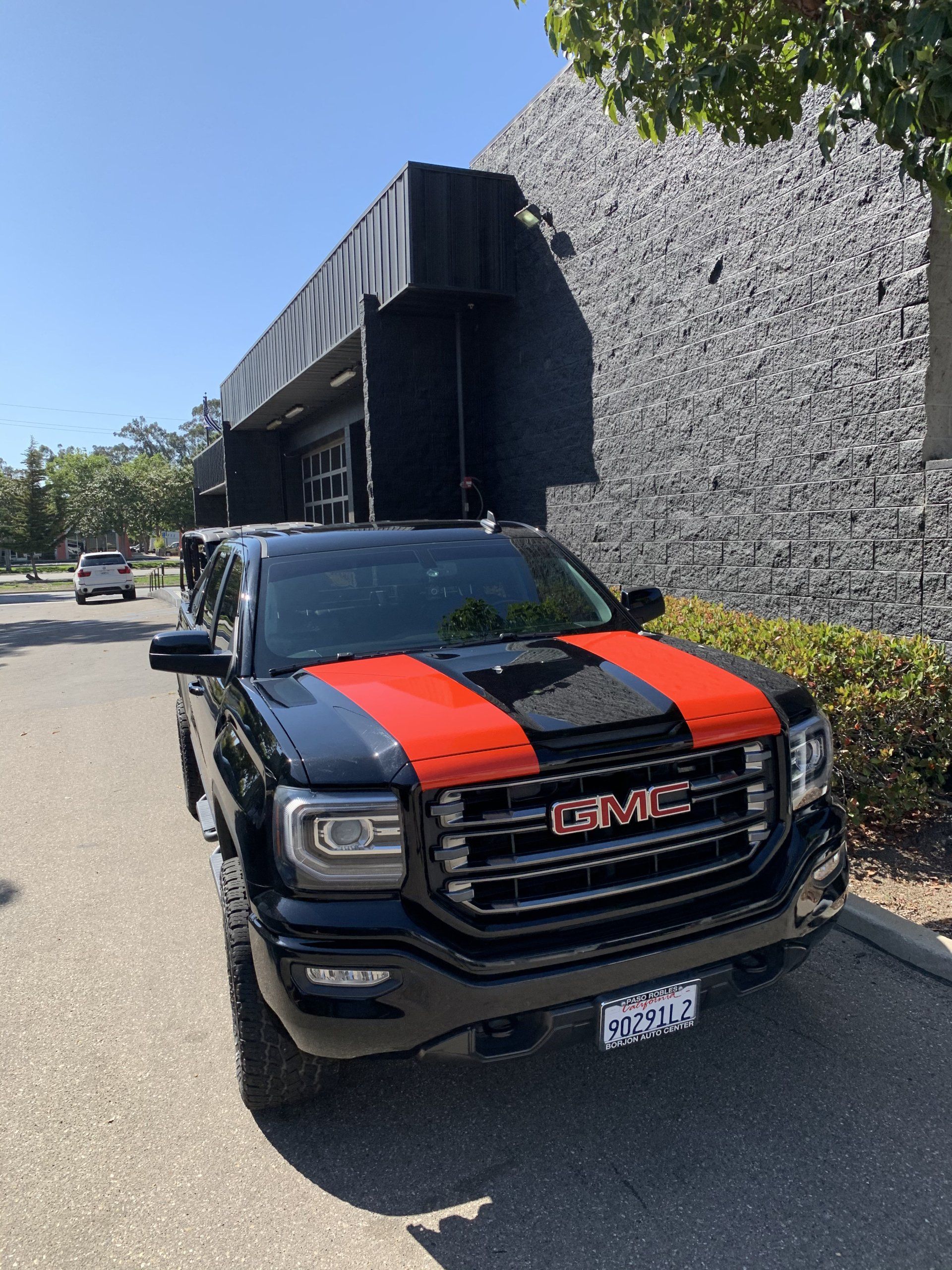 Black GMC pickup with red racing stripes parked outside a modern building on a sunny street