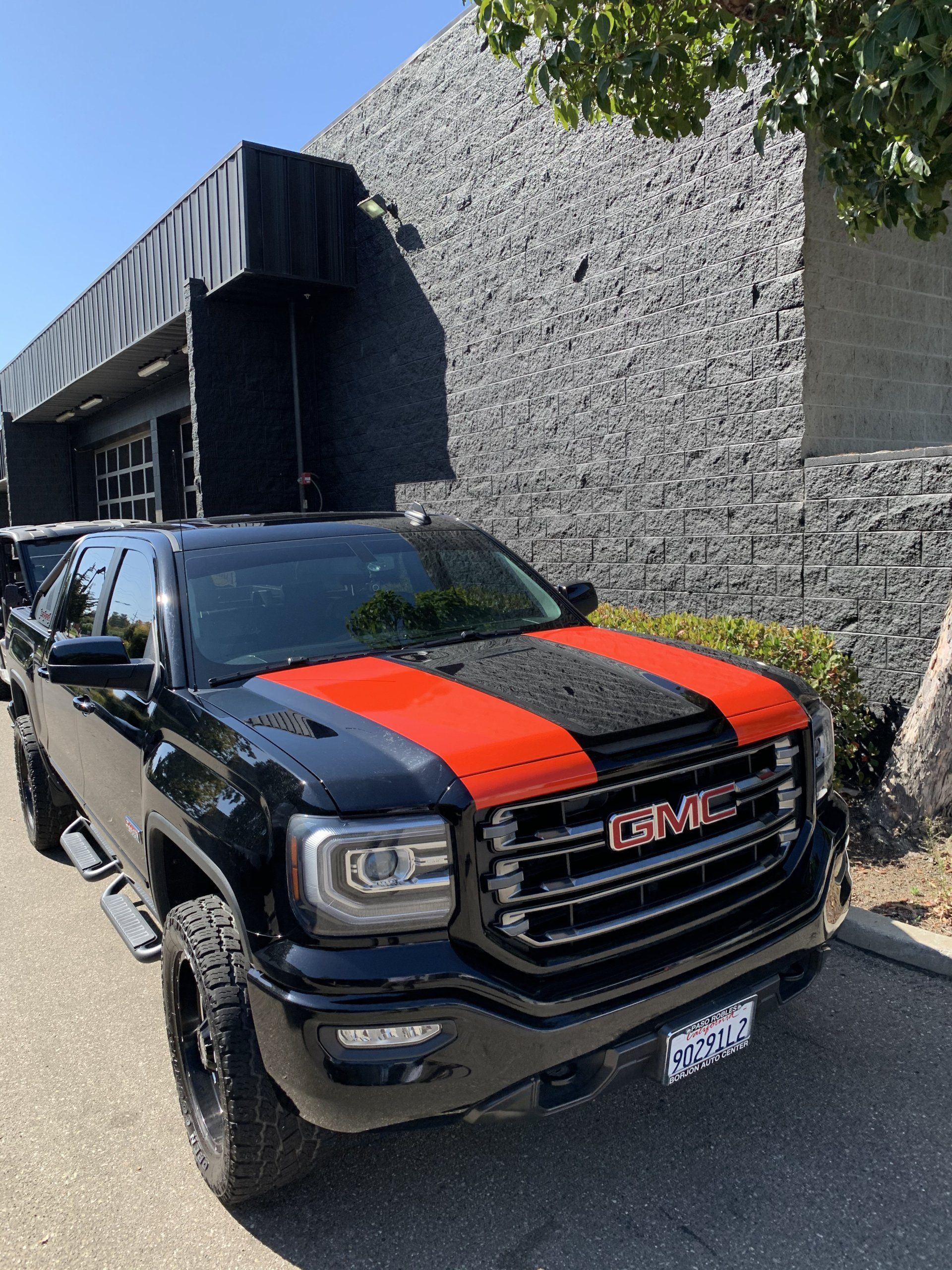 Black GMC truck with red racing stripes parked beside a gray stone building.