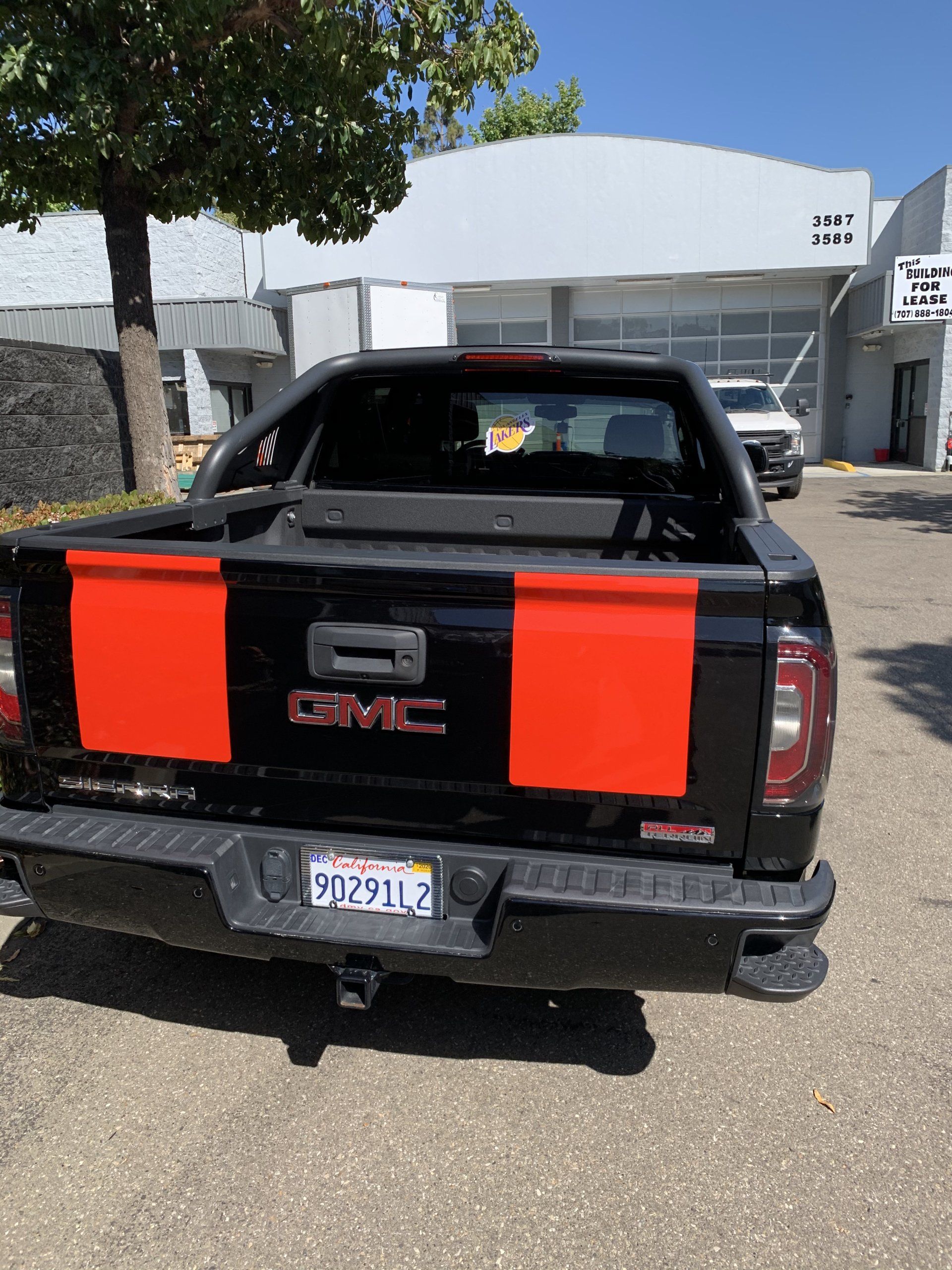Black GMC pickup with red tailgate panels parked outdoors near a building.