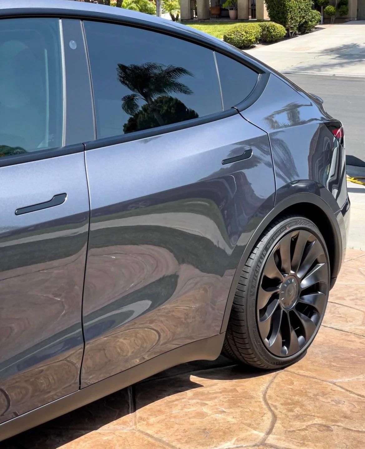 Gray Tesla SUV parked on a driveway, showing the rear side and black wheel.