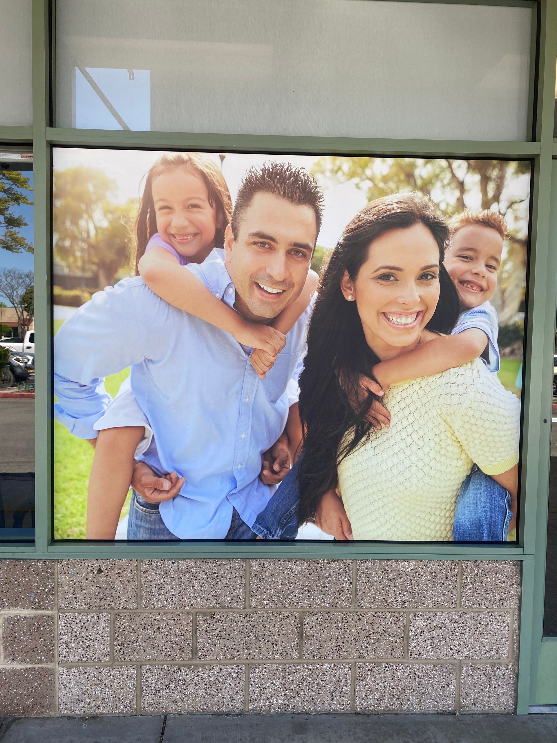 Smiling family portrait displayed in a window storefront with a stone wall below.
