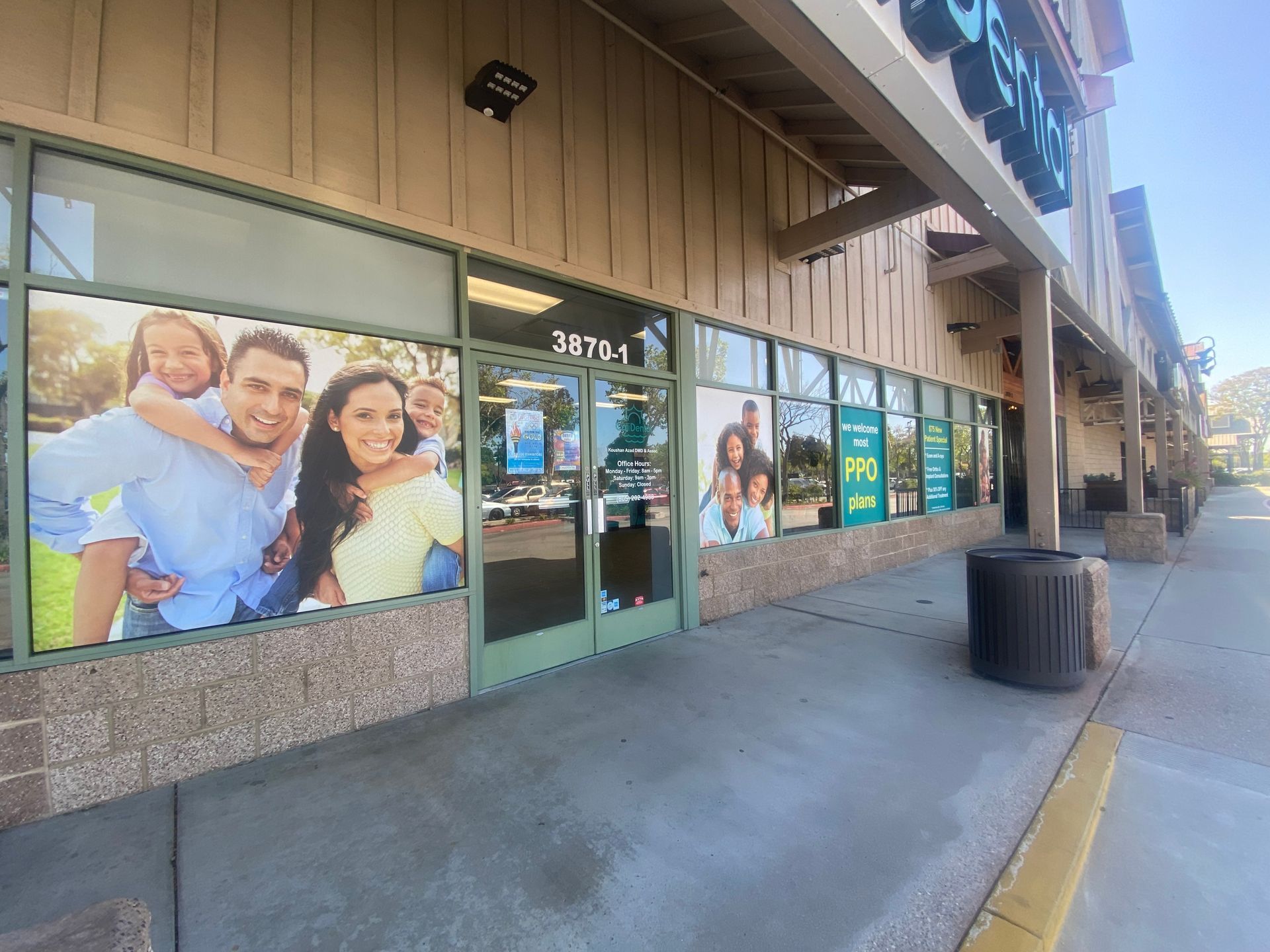 Storefront with glass windows, a door, and a family photo mural along a shopping center walkway.