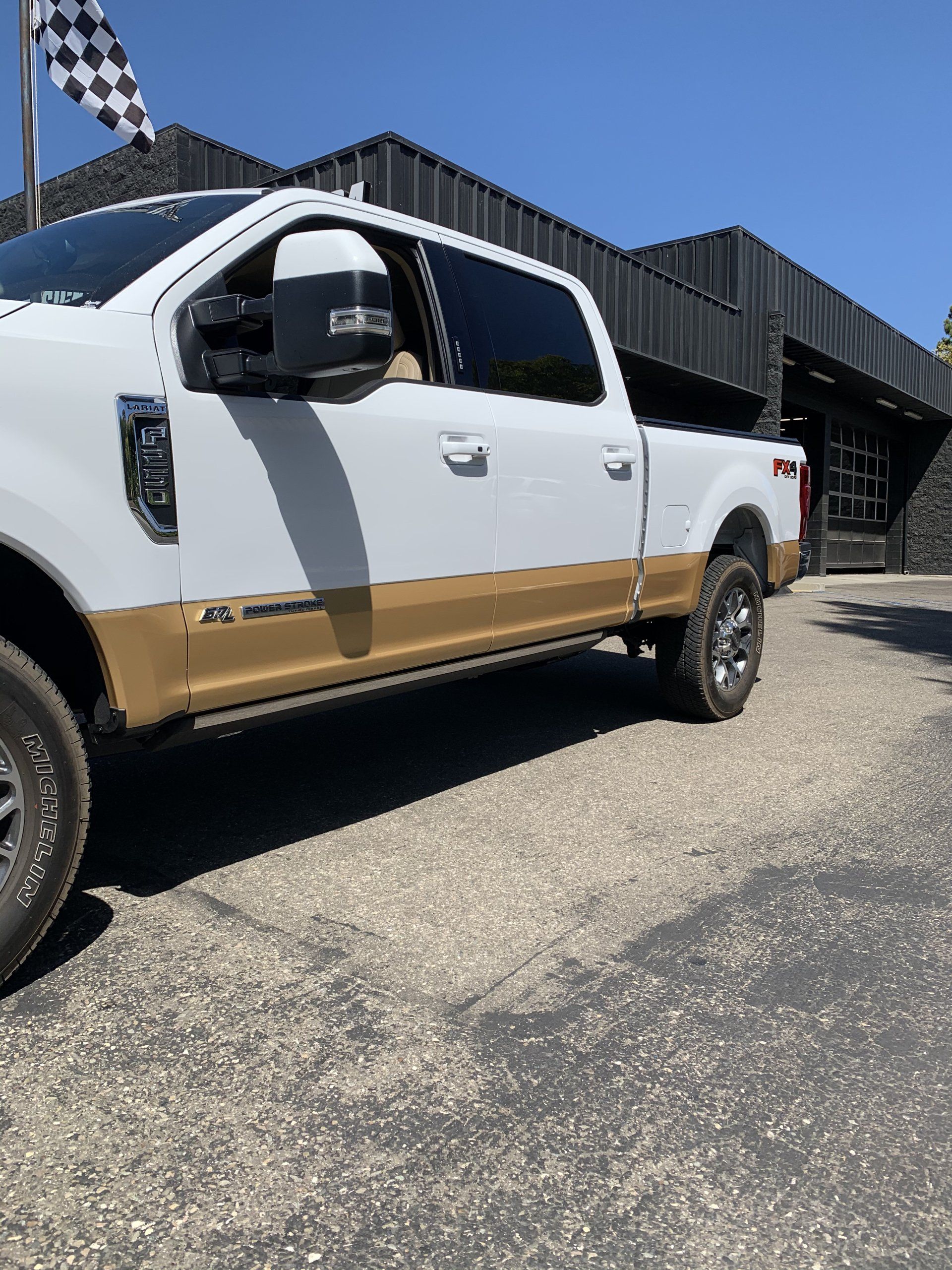 White and tan pickup truck parked outside a building on a sunny day