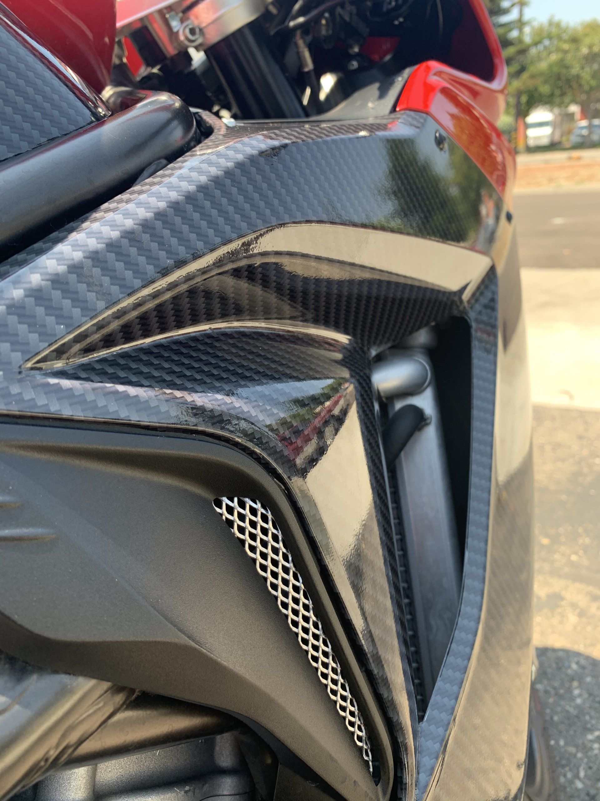 Close-up of a glossy carbon fiber vehicle body panel with black mesh vent and red trim