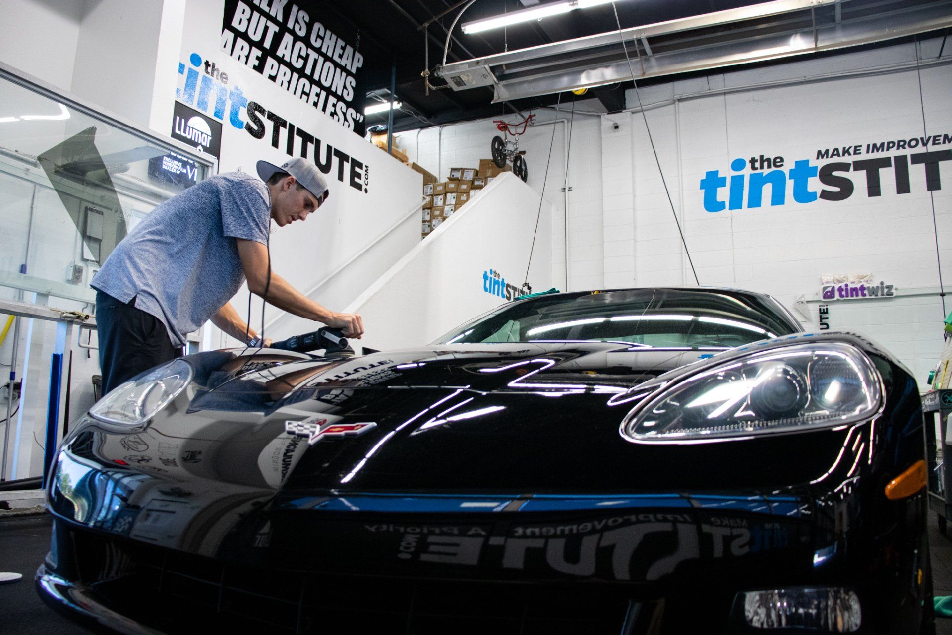 Technician applying window tint to a black sports car in a garage workshop
