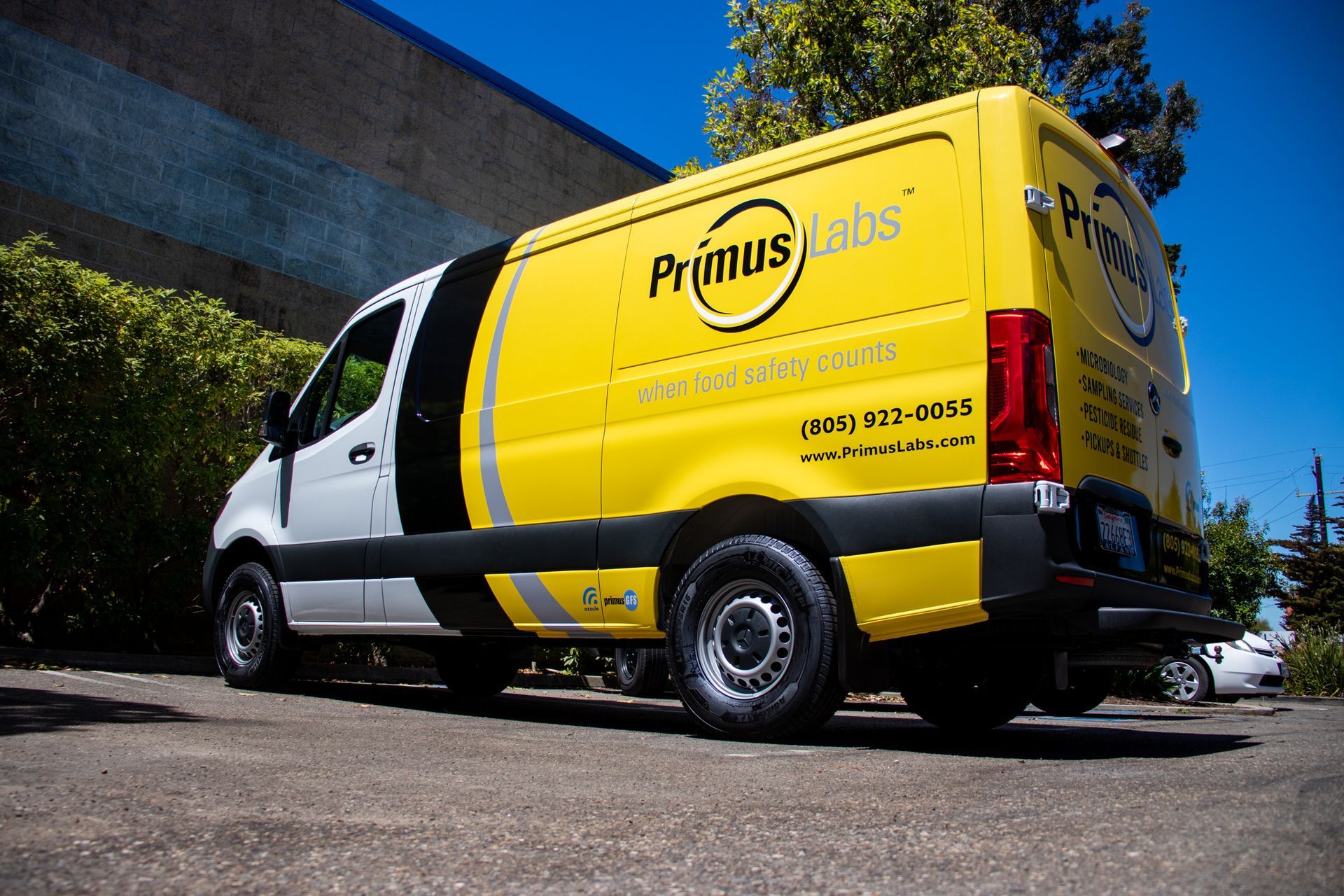 Yellow Primus Labs van parked outside a building on a sunny street.