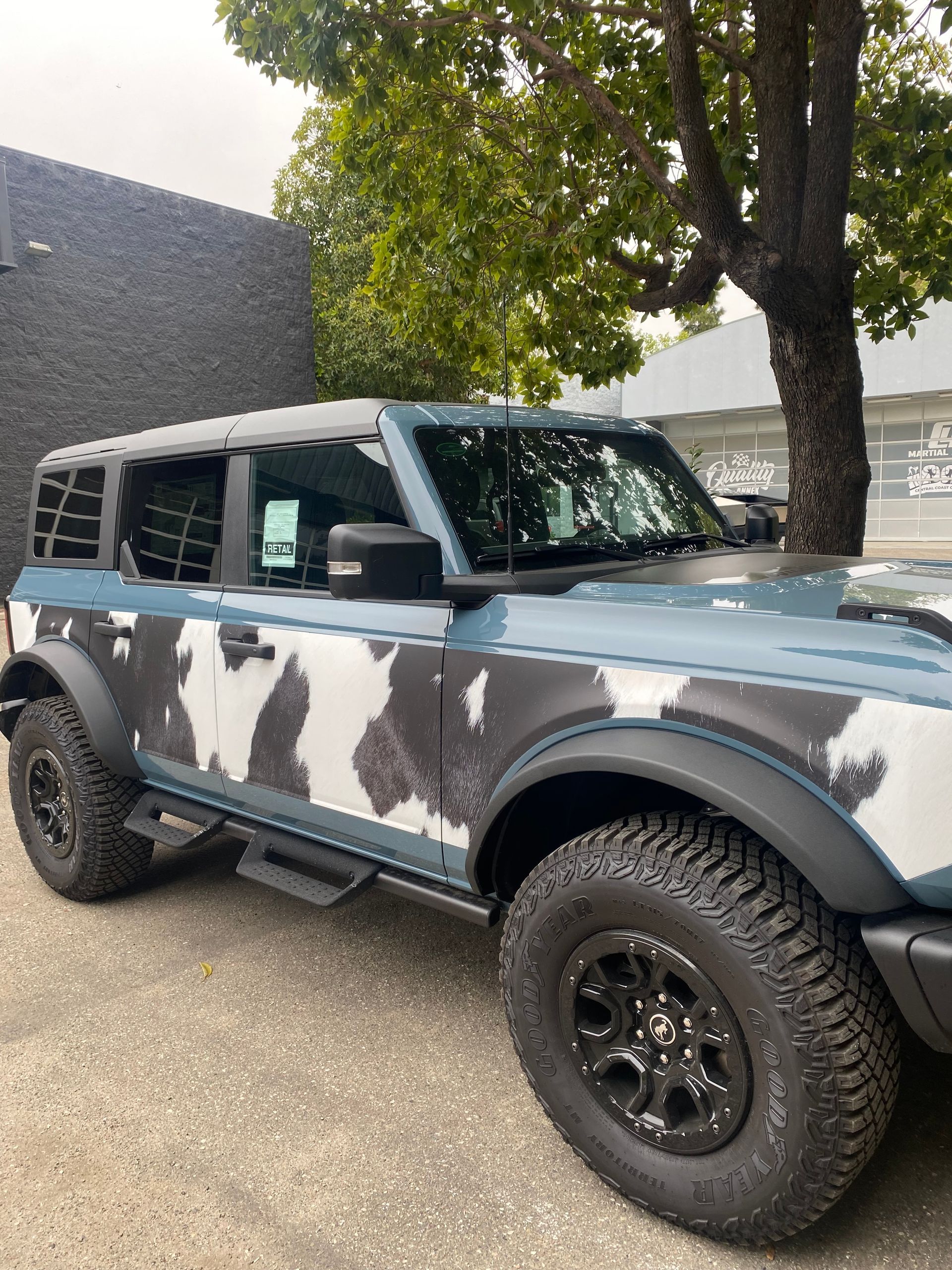 Camouflaged off-road SUV parked beside a tree on a paved lot