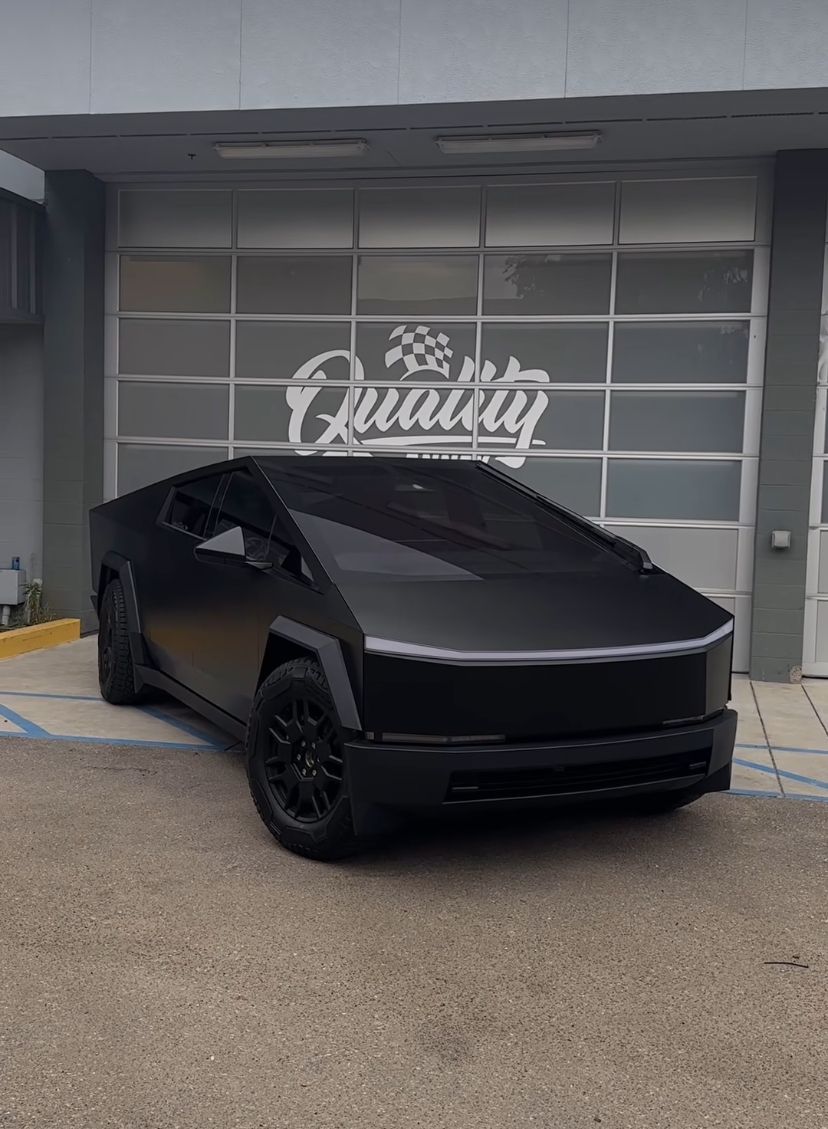 Matte black futuristic SUV parked in front of a garage with a “Quality” sign.