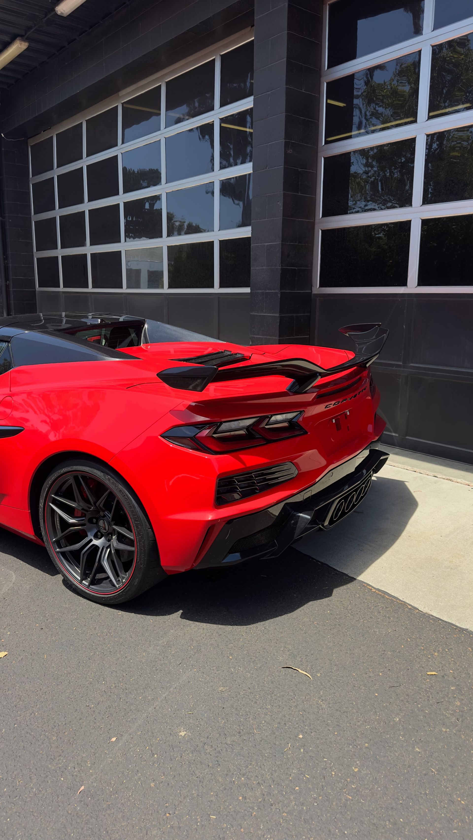 Red sports car parked beside a building with large black-framed windows.