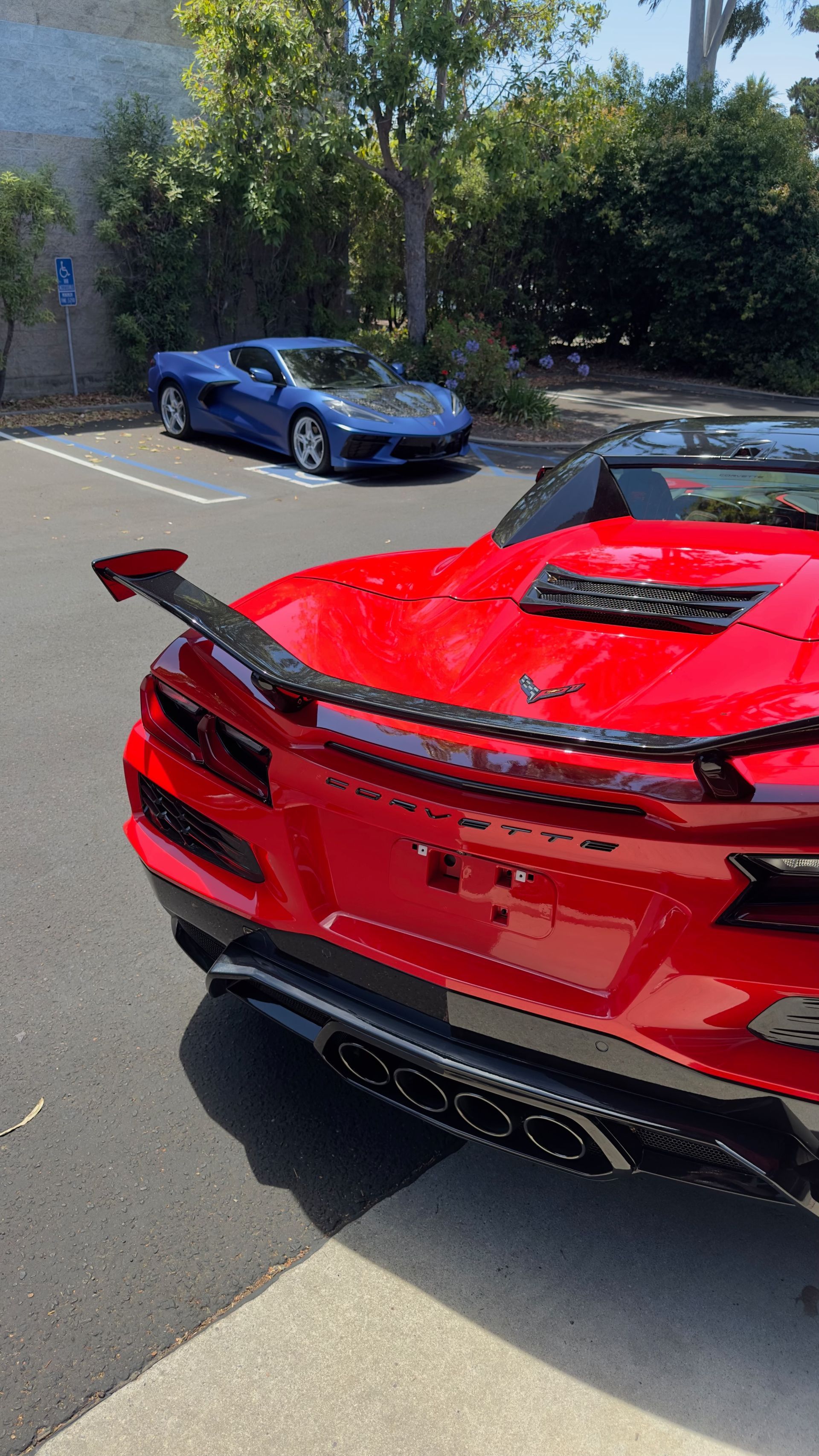 Red sports car in foreground with blue sports car parked behind on a sunny street.