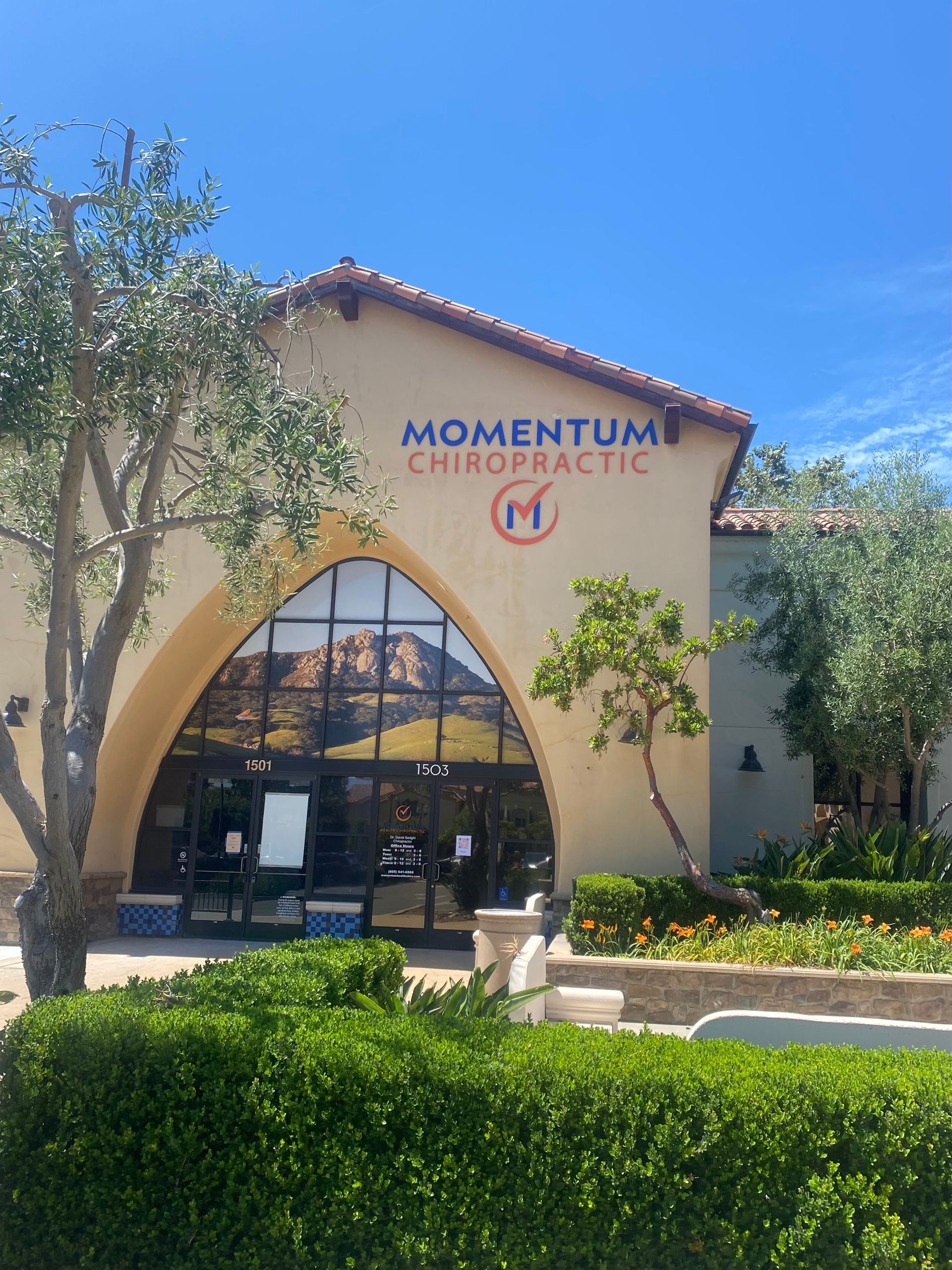 Momentum Chiropractic storefront with arched entrance, blue sign, and desert landscaping under a clear sky