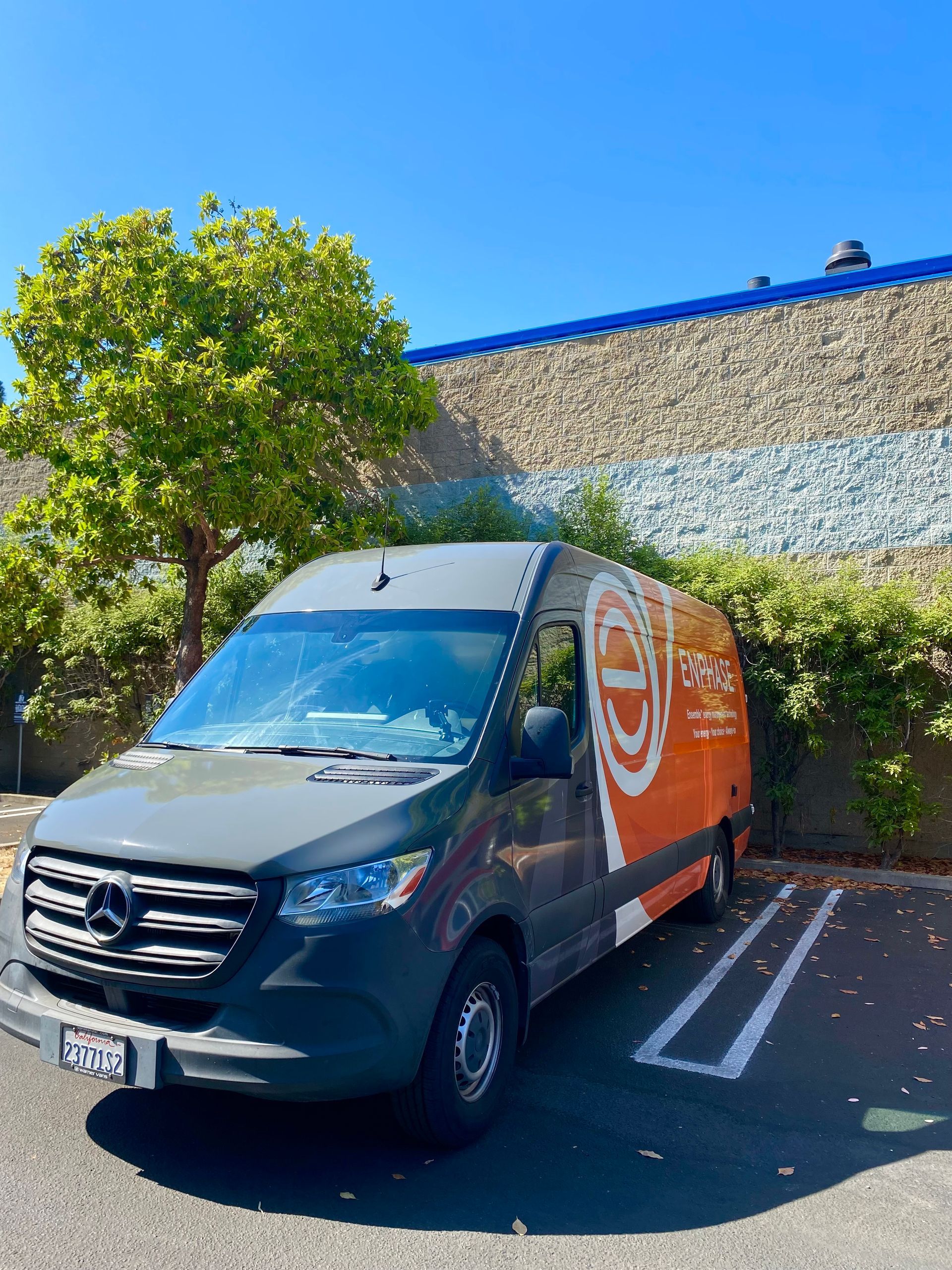 Black delivery van with orange side panel parked outside a building under a bright blue sky
