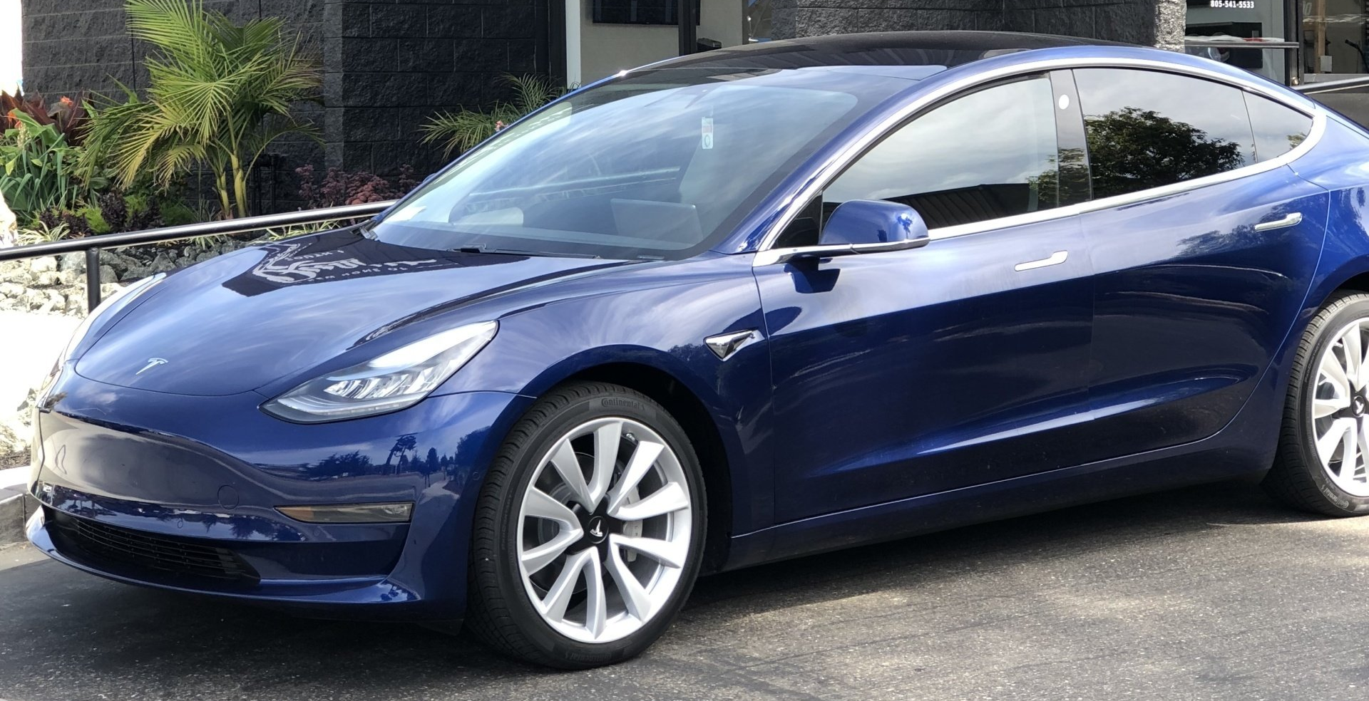 Blue Tesla sedan parked outdoors in sunlight, side view