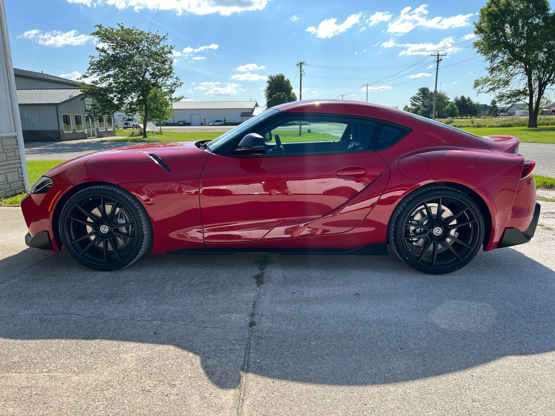 Red sports coupe parked on a sunny street, with black wheels and a blue sky background