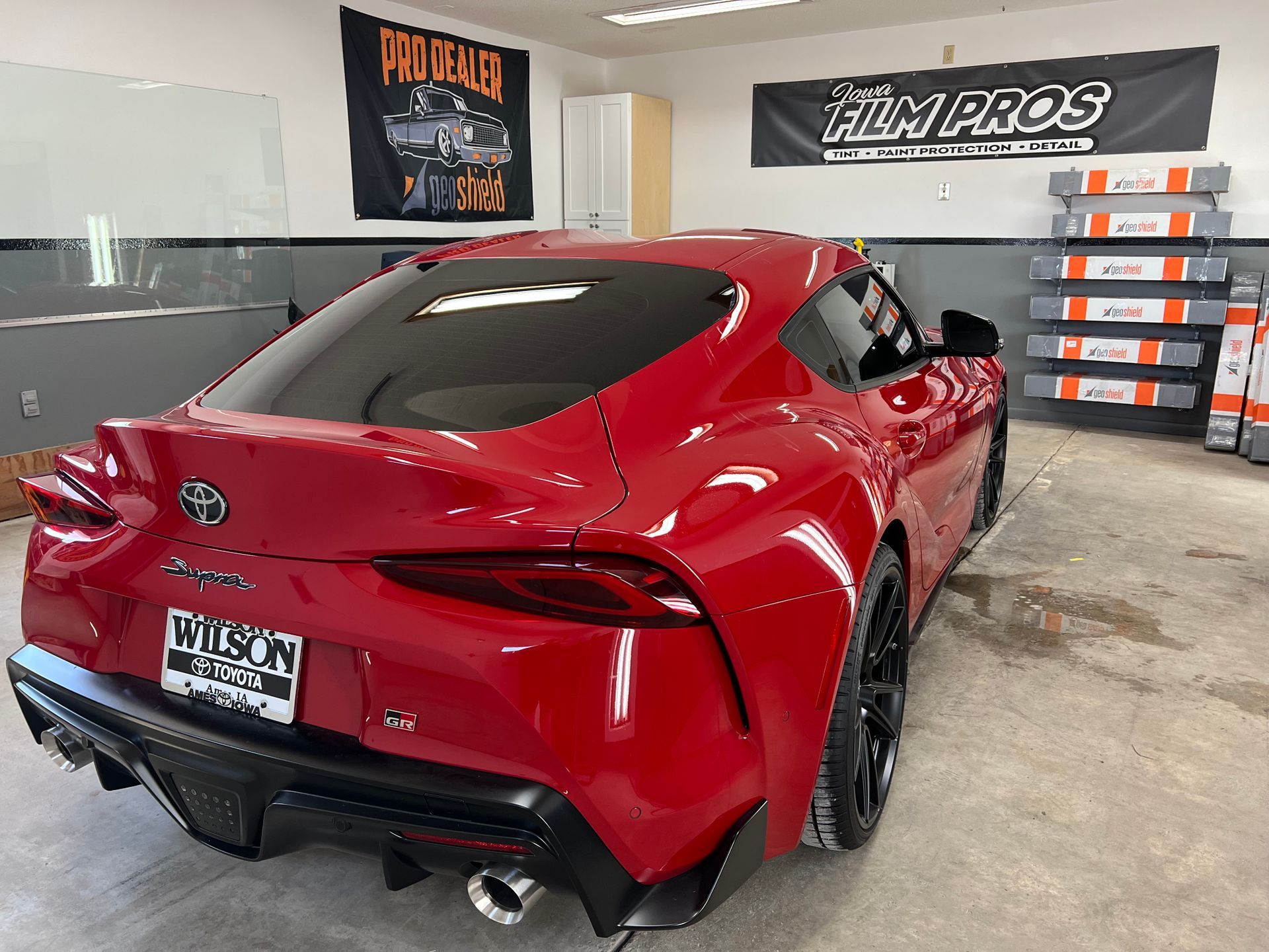 Red sports car parked inside a garage with wall banners and tire stacks