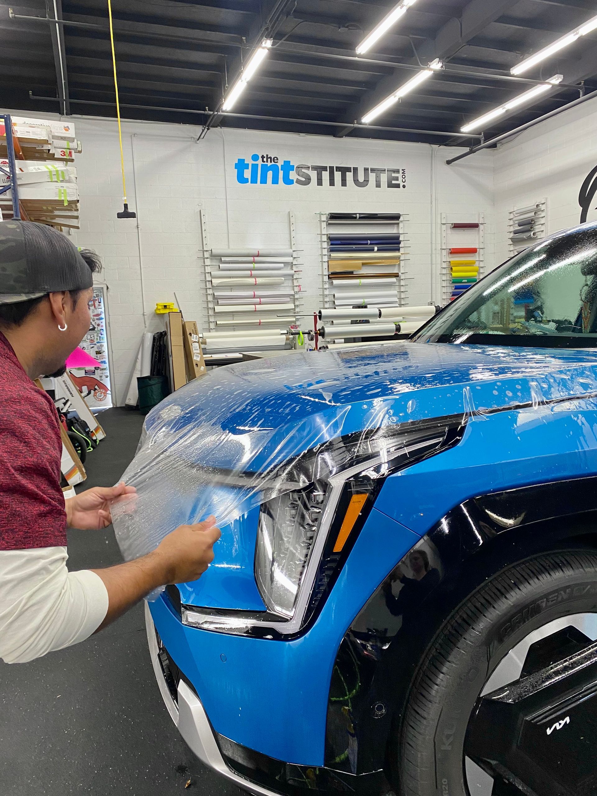 Technician applying blue vinyl wrap to a blue SUV in a workshop
