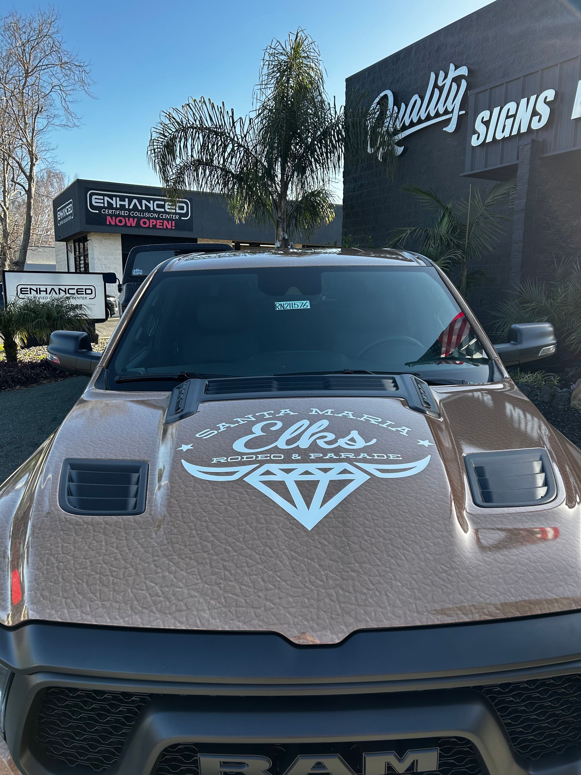 Customized truck with a graphic hood decal parked outside a business sign reading “Signs”
