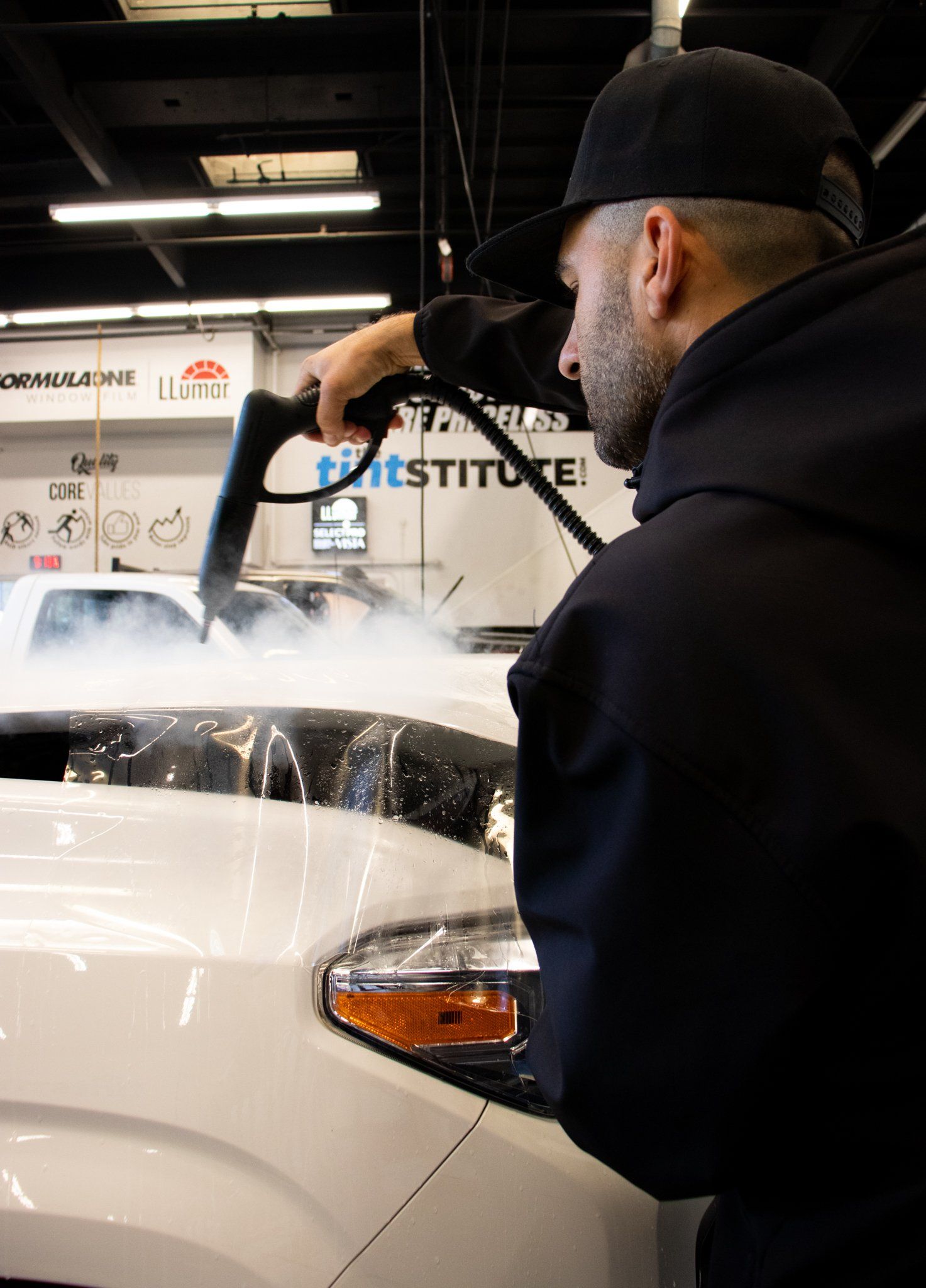 A person using a power tool to polish a white car in an auto shop
