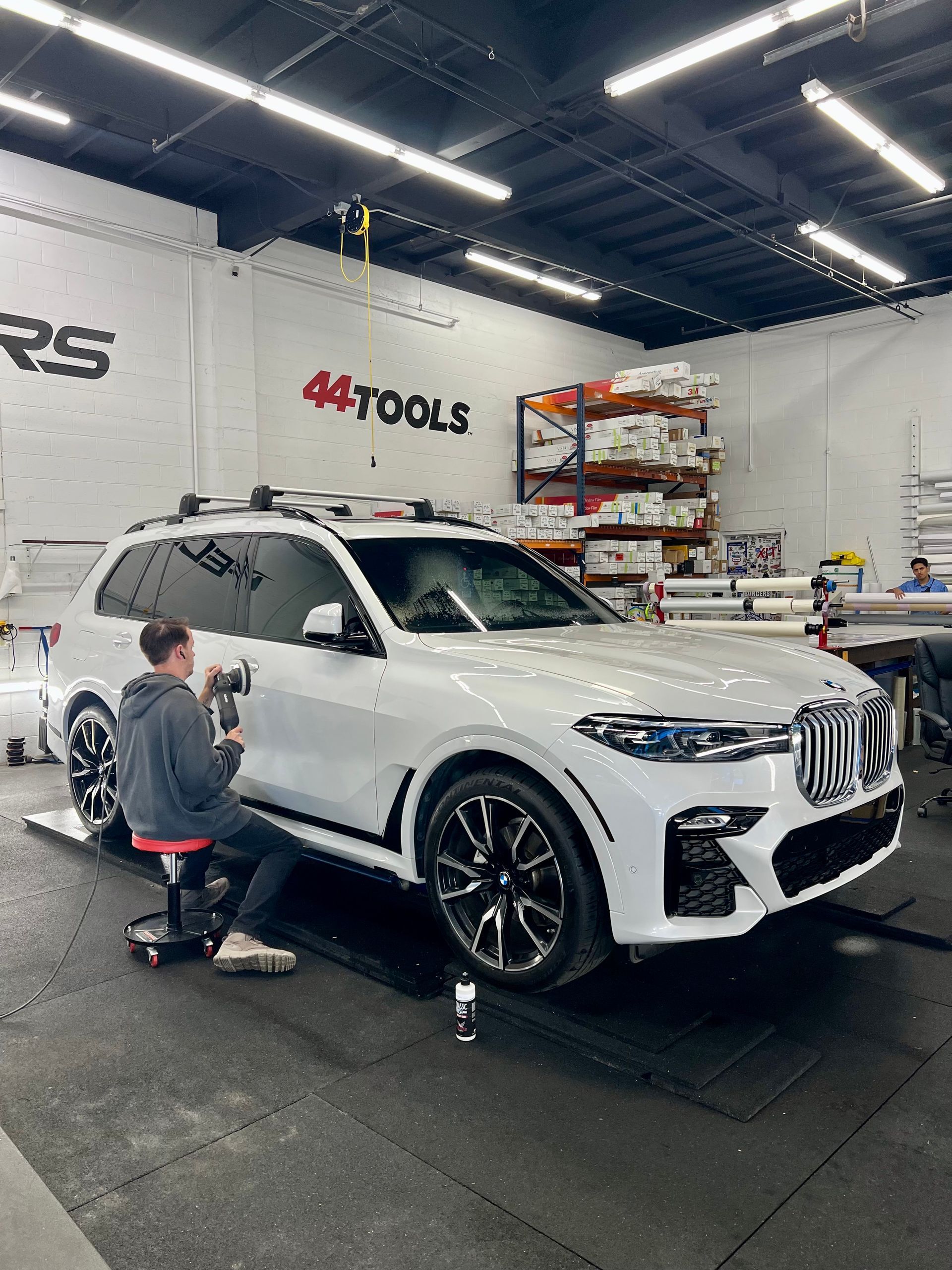 White SUV in an auto shop while a mechanic works near the front wheel.