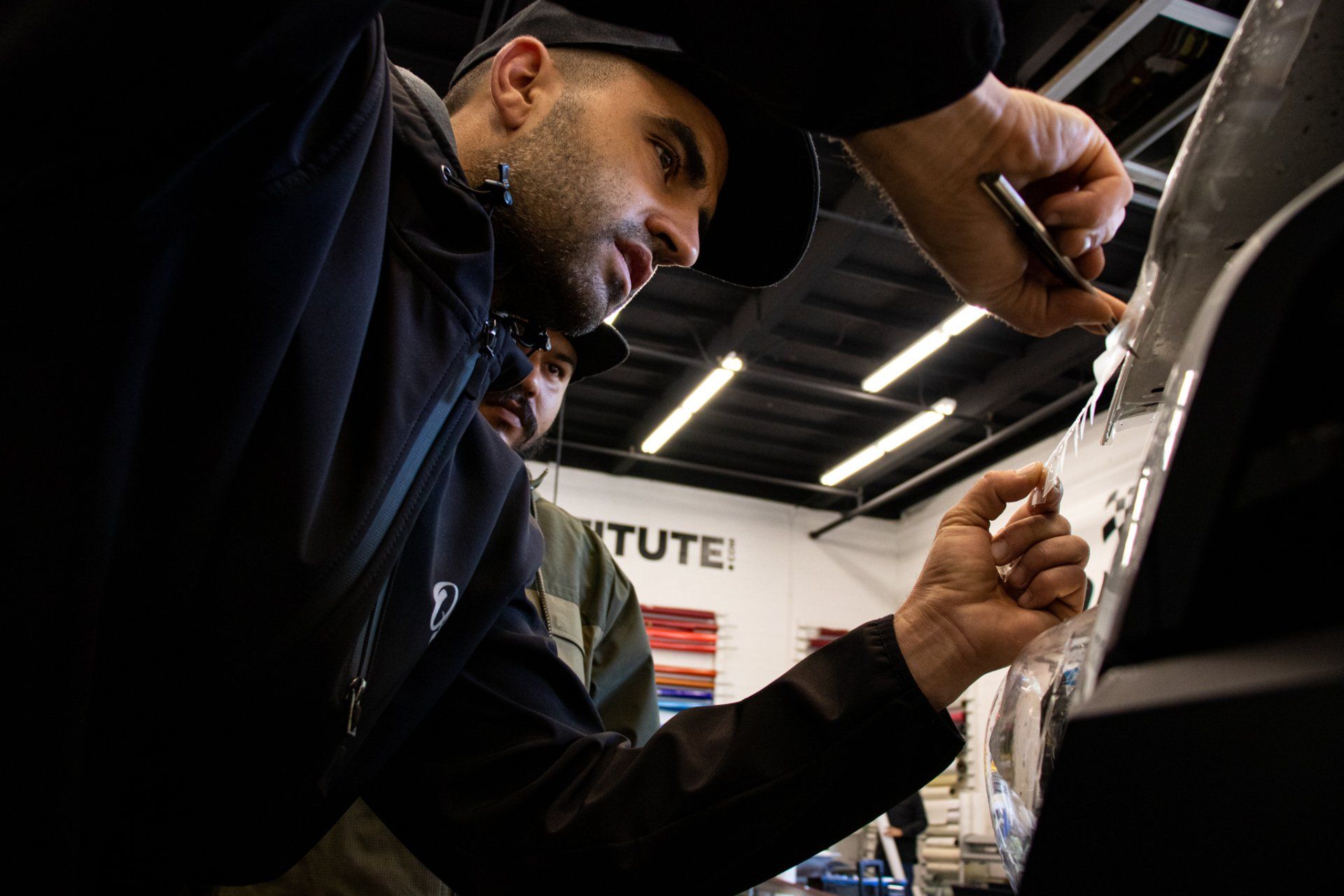 Two people working on a car in a garage, one using a tool near the hood.