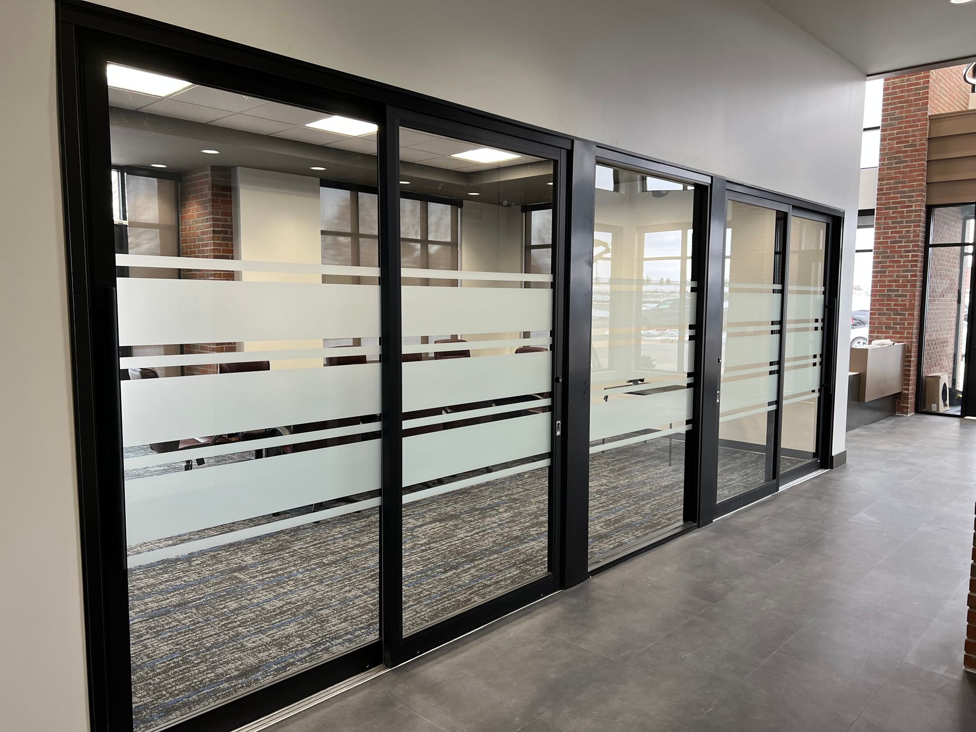 Glass-walled office hallway with frosted stripes along a covered outdoor walkway