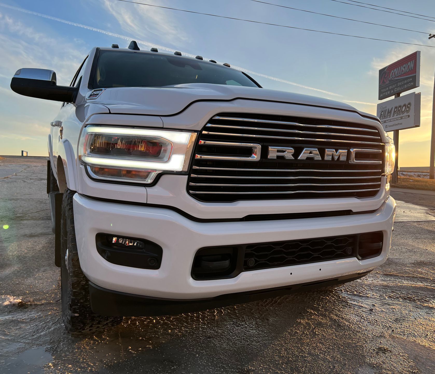 White RAM pickup truck parked outdoors at dusk, front grille and headlights visible.