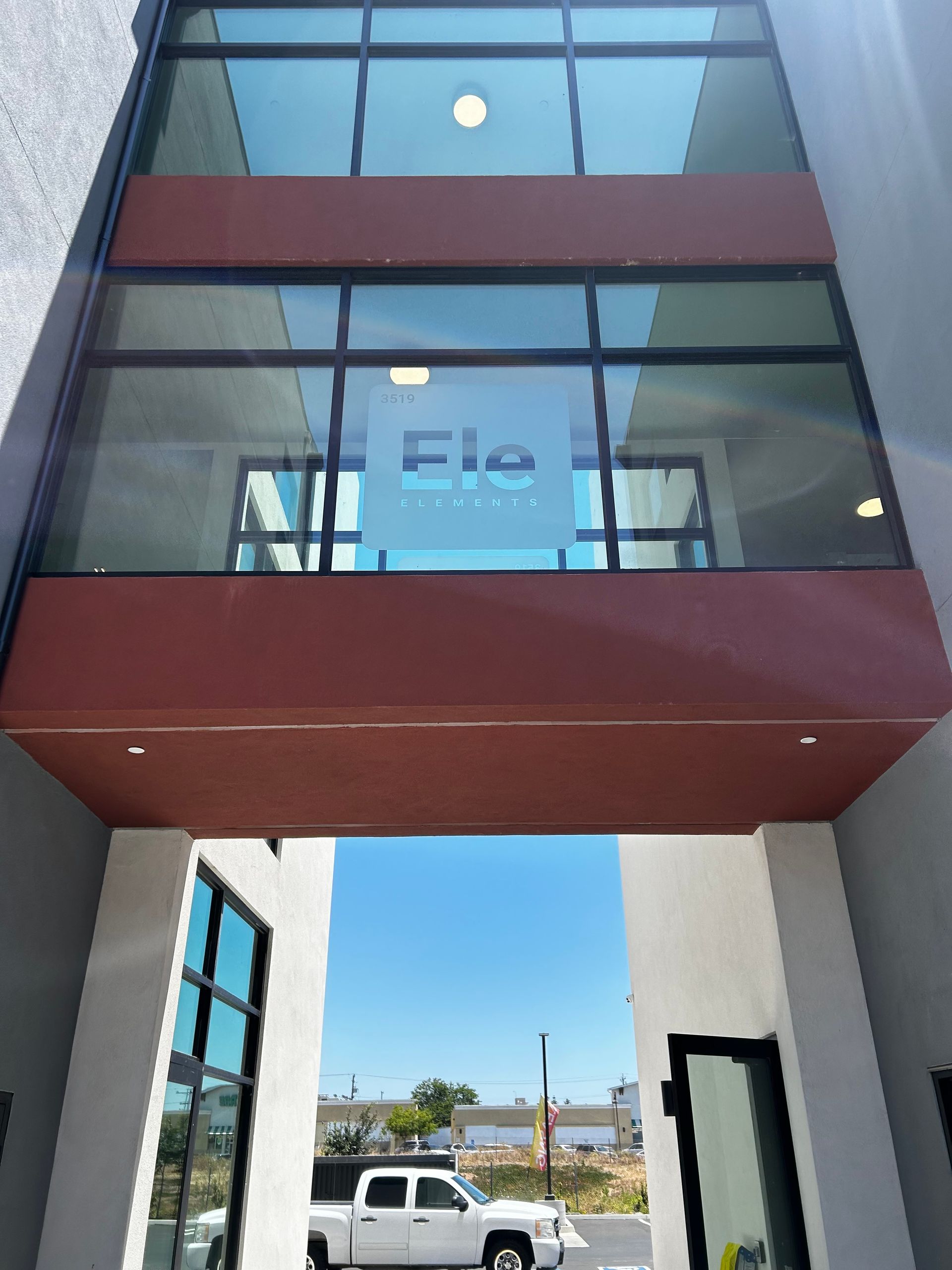 Glass-front building entrance with red panels, viewed from below through a covered walkway.