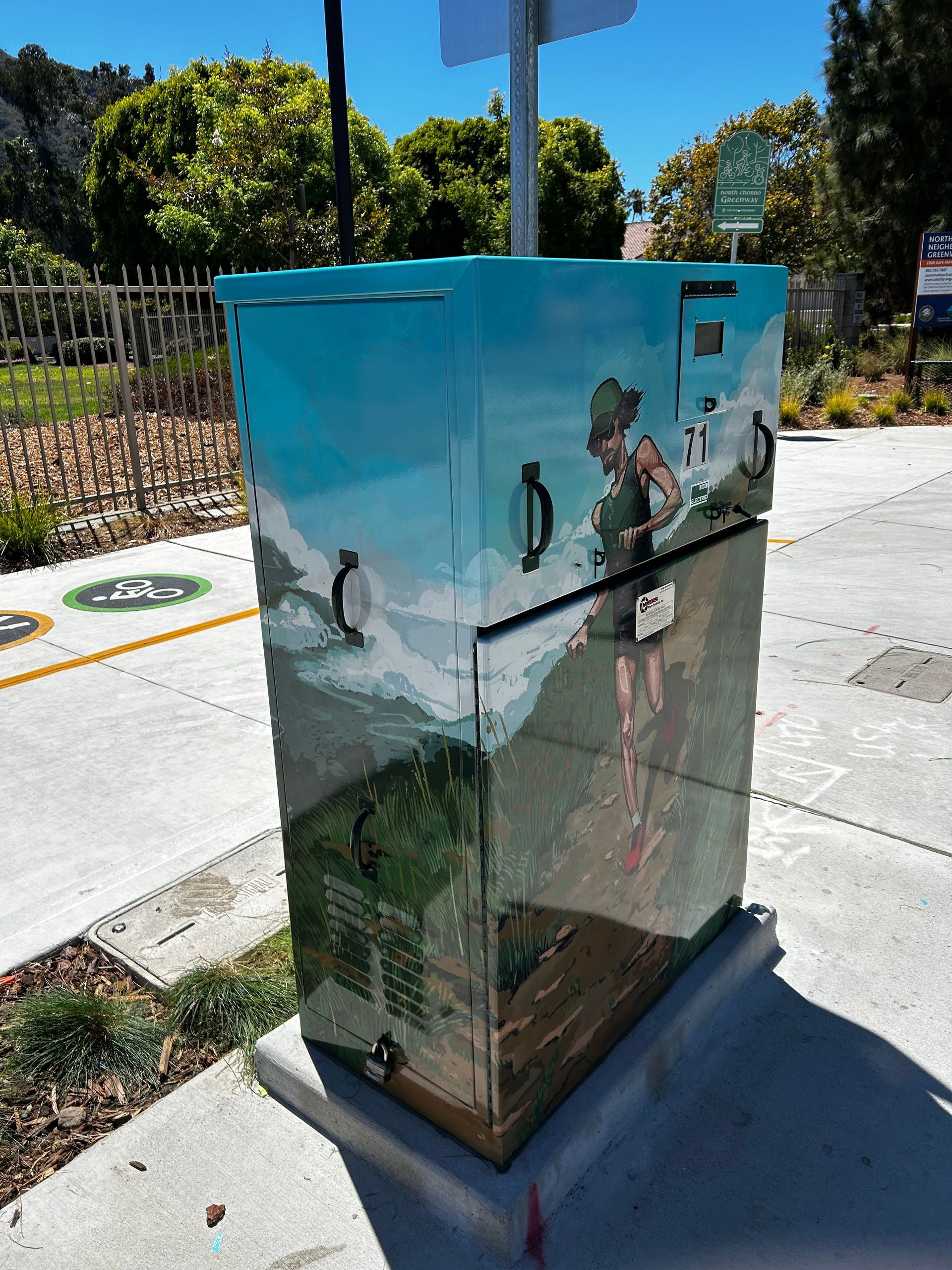 Painted utility box with a marine mural on a sunny sidewalk near trees and parking lines