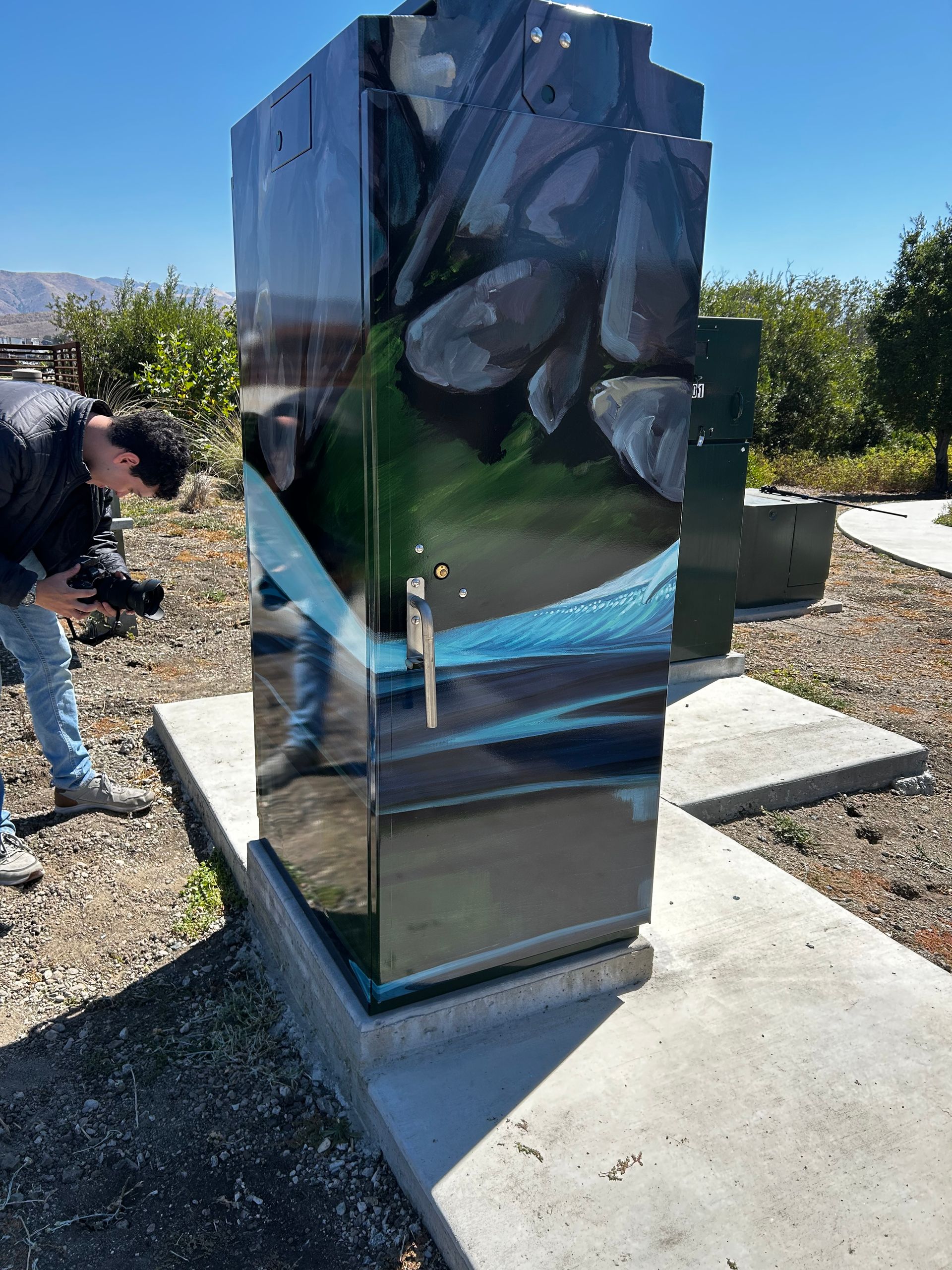 Reflective black stone monument outdoors on a concrete base, with a person partially visible beside it.