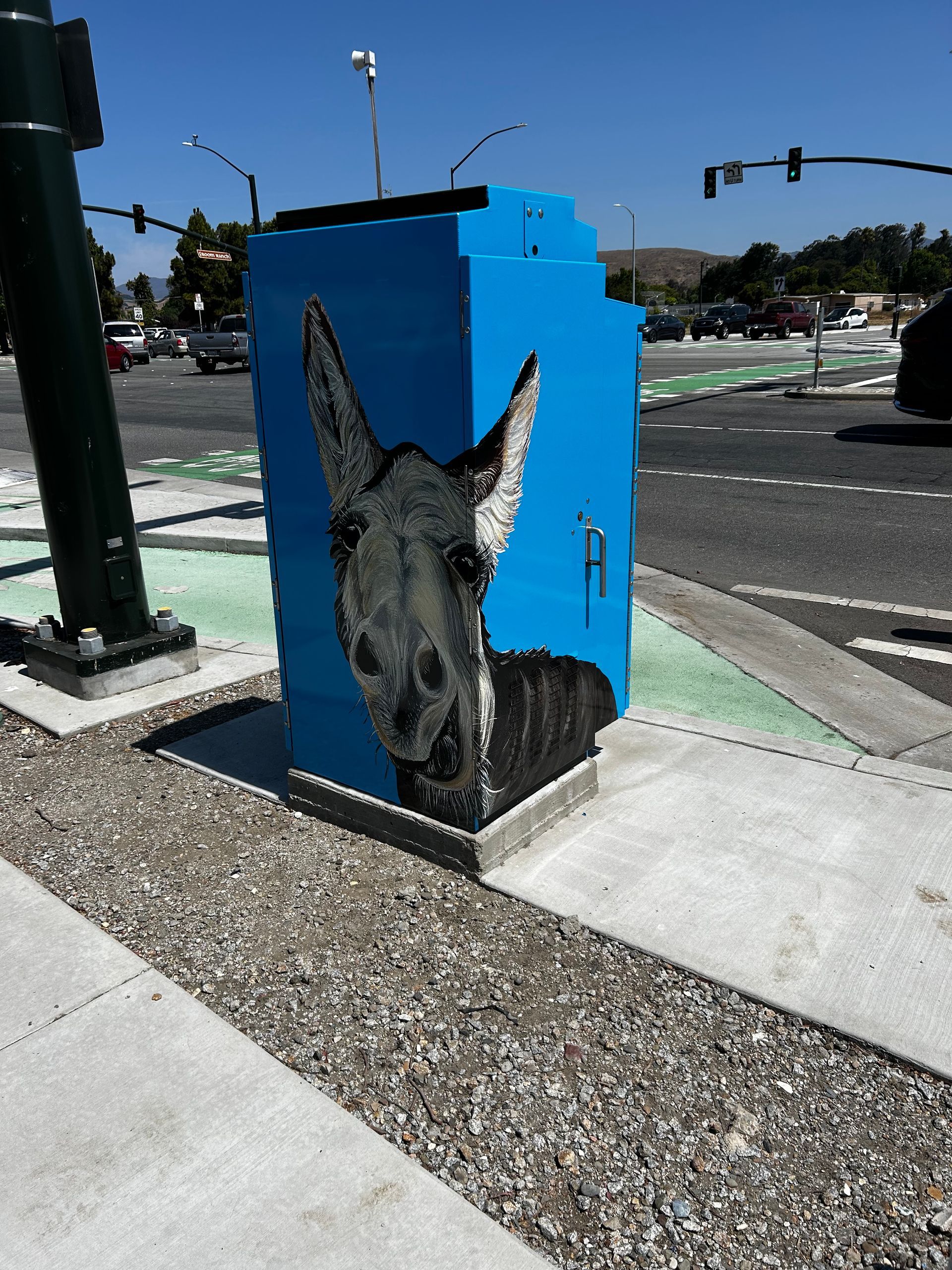 Blue utility box with a black-and-white donkey mural on a sunny street corner