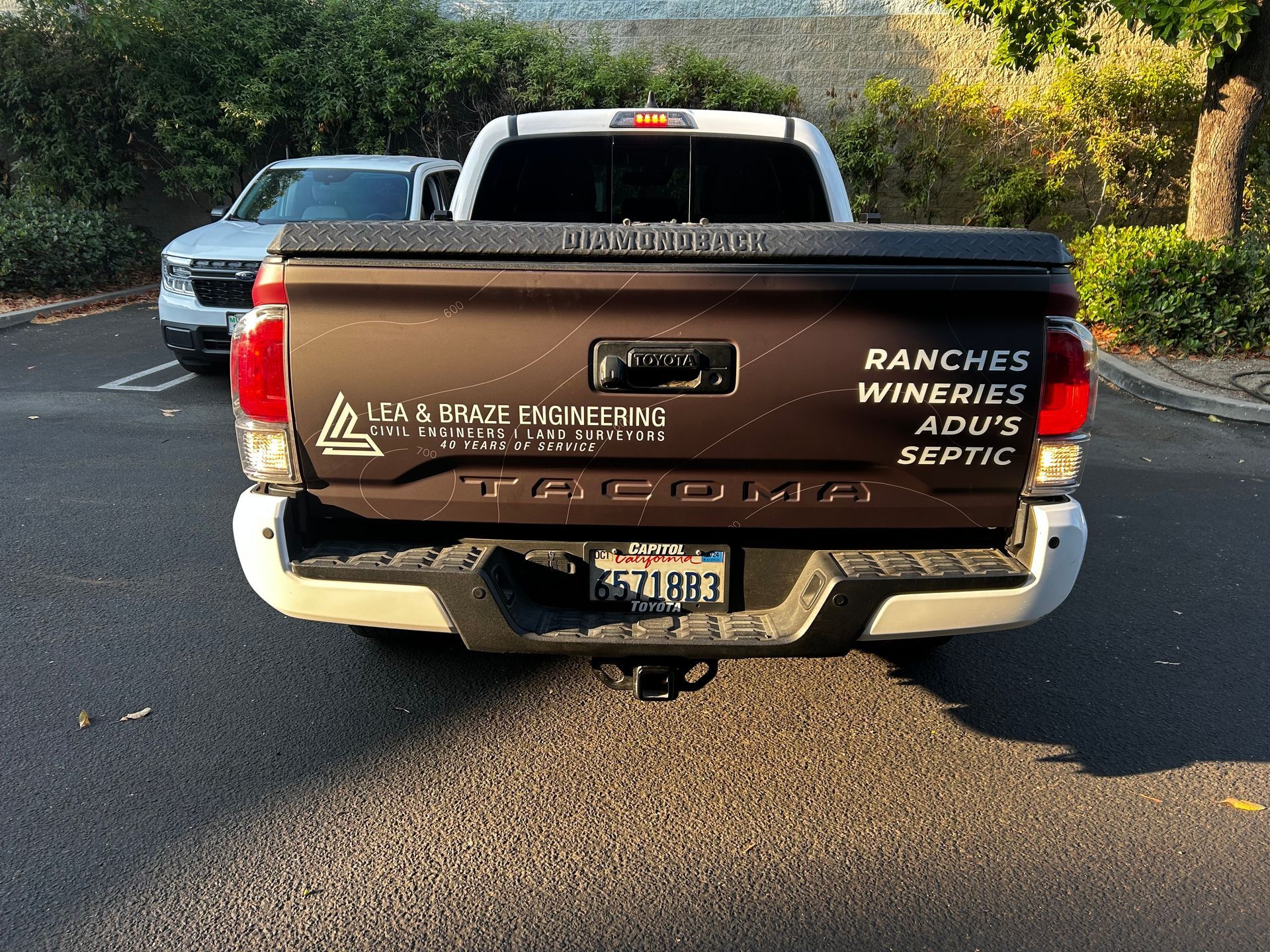 Rear view of a brown pickup truck with company logos parked on a sunlit street.