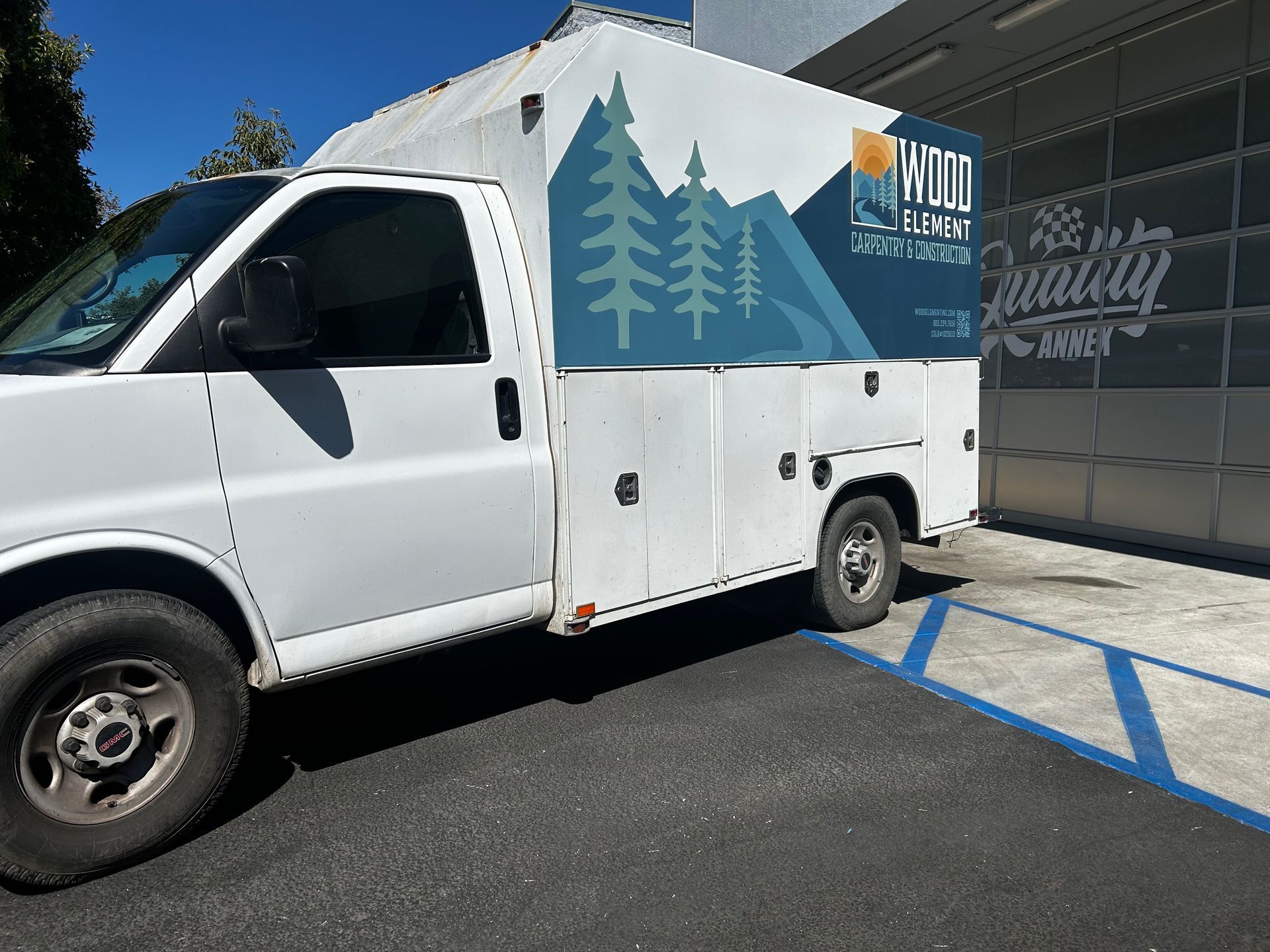 White utility truck with blue tree graphics parked in a marked accessible spot beside a building.