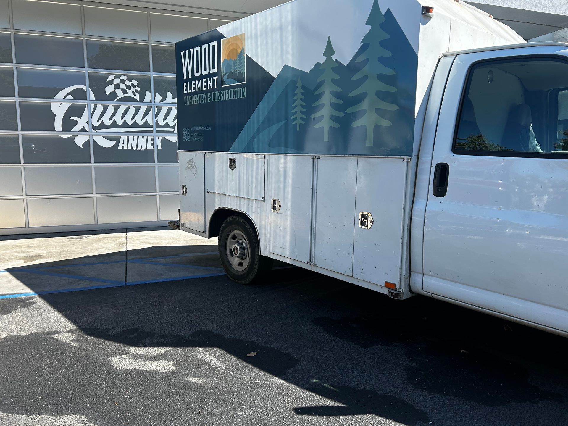 White utility truck with tree mural parked beside a building with a Quanz logo.