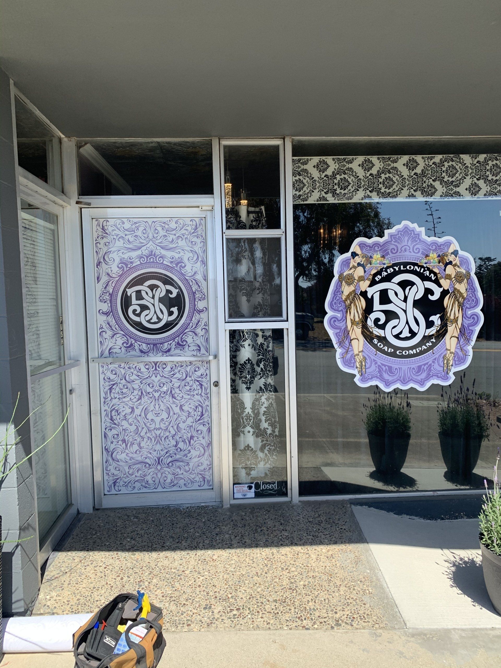 Storefront entrance with purple decorative window decals and a potted plant by the glass door.