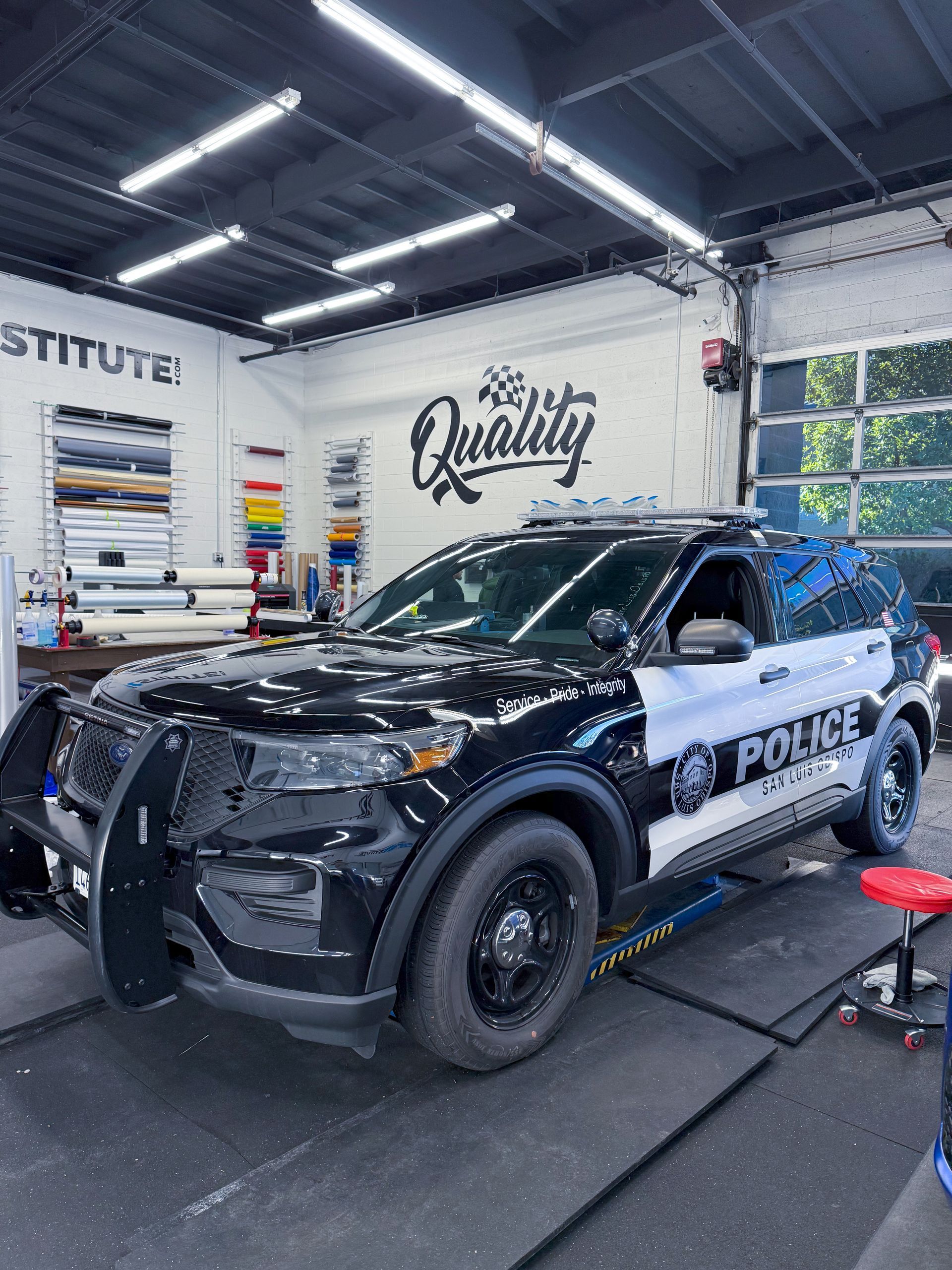 Black police SUV in an auto detailing shop, with polishing lights and tools visible in the background