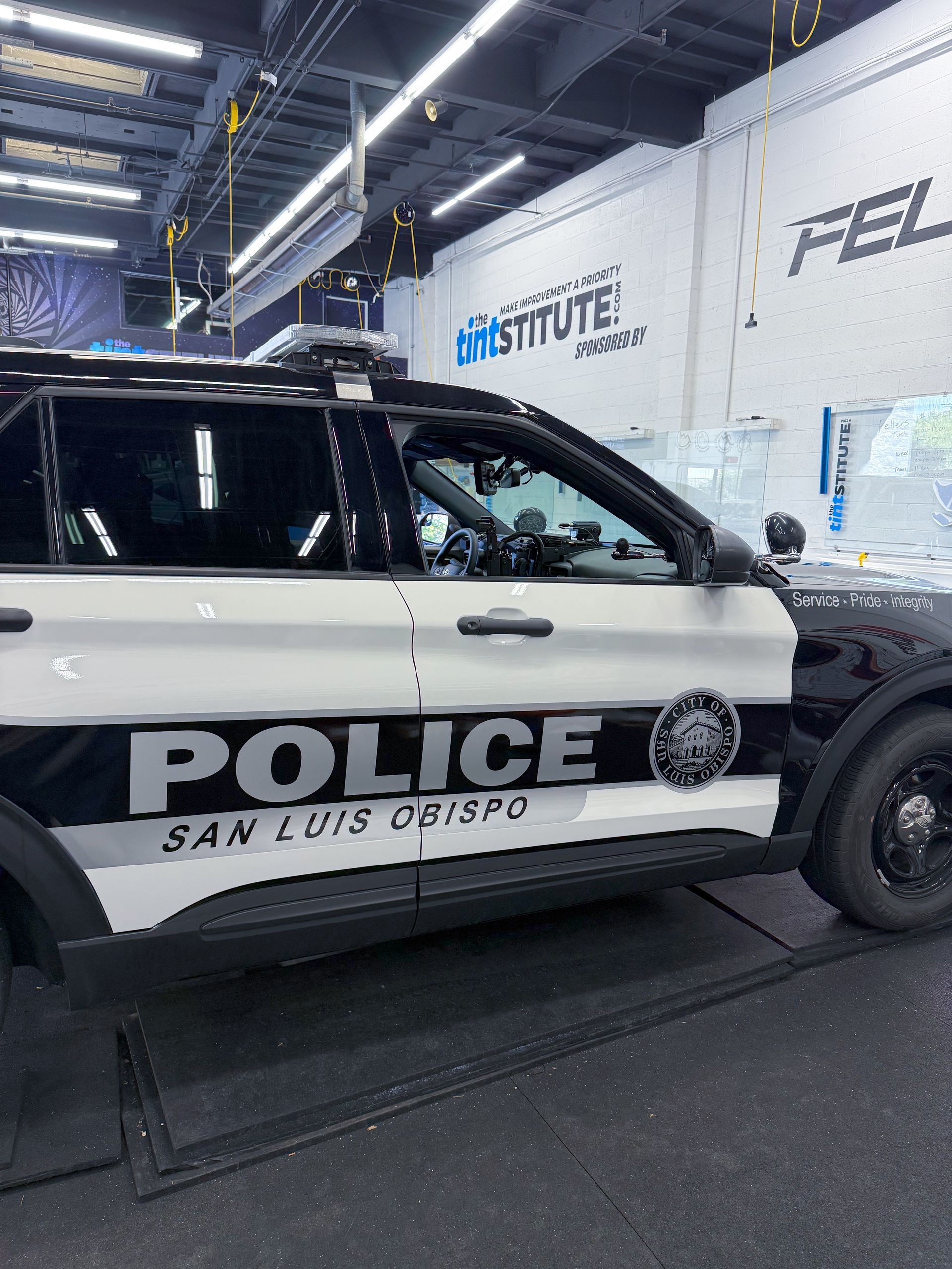 San Luis police SUV parked indoors beside a wall with company logos and a black-and-white livery