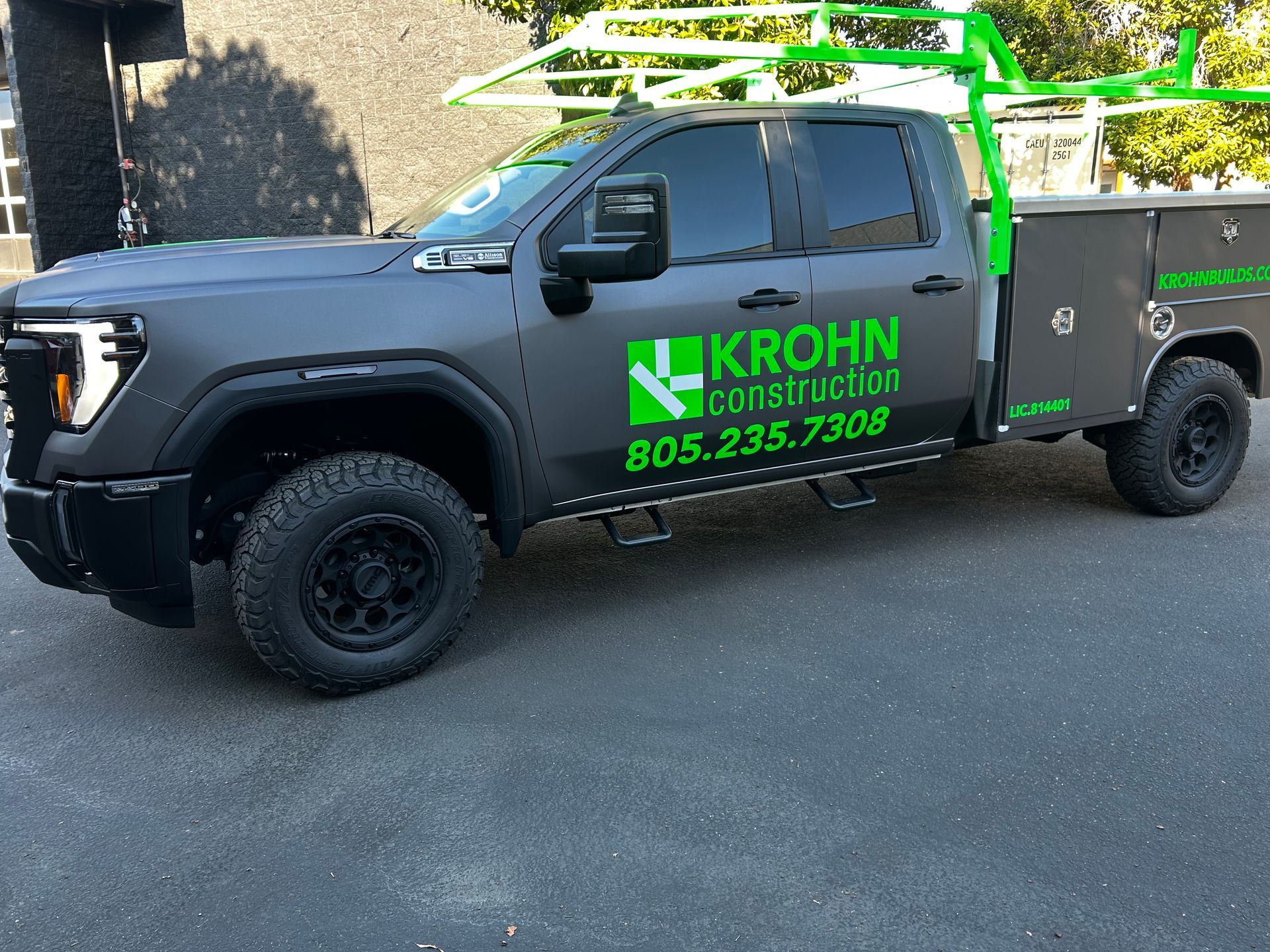 Black Krohn Construction pickup truck with green ladder rack parked on a street