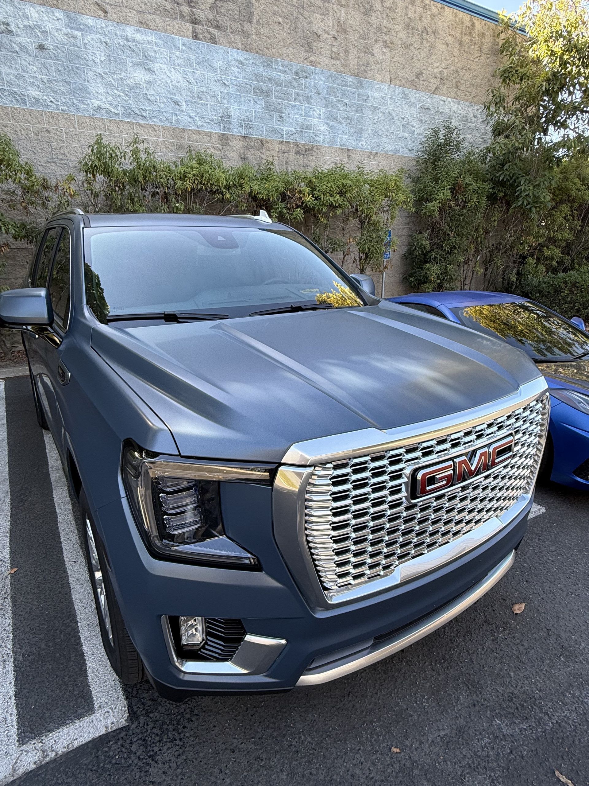 Gray GMC SUV parked in a lot beside a wall with greenery