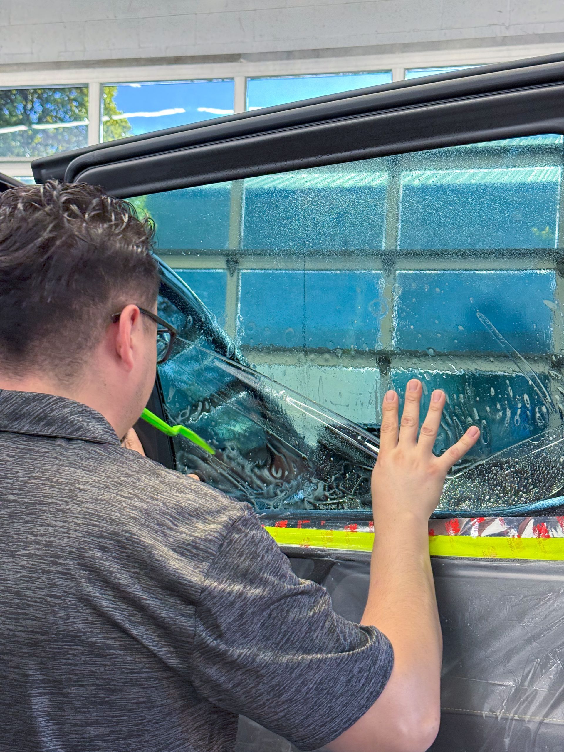 Person leaning on a car window with a shattered blue pane and yellow tape nearby