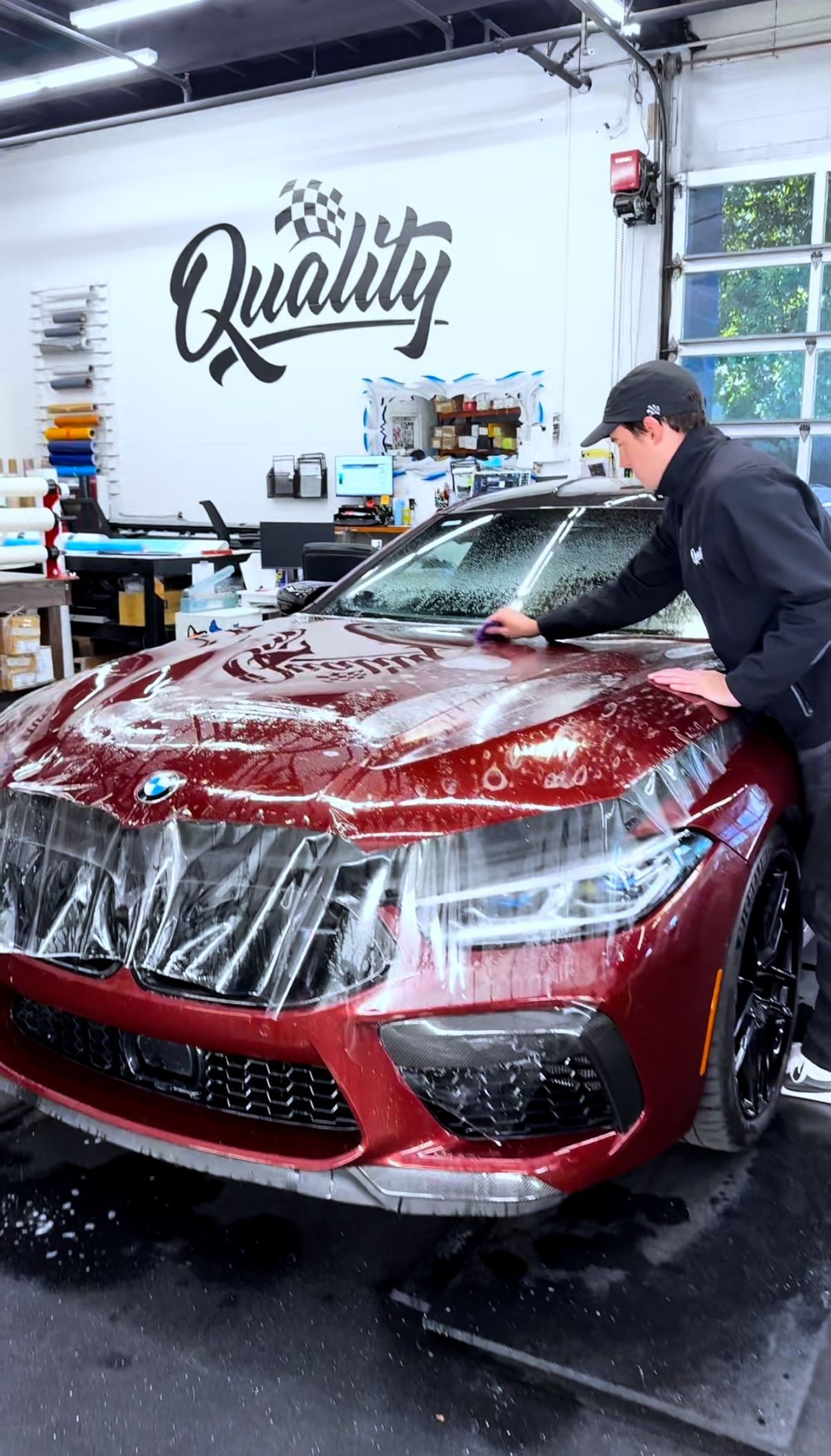 Detailer washing a red car in a garage with a “Quality” sign on the wall