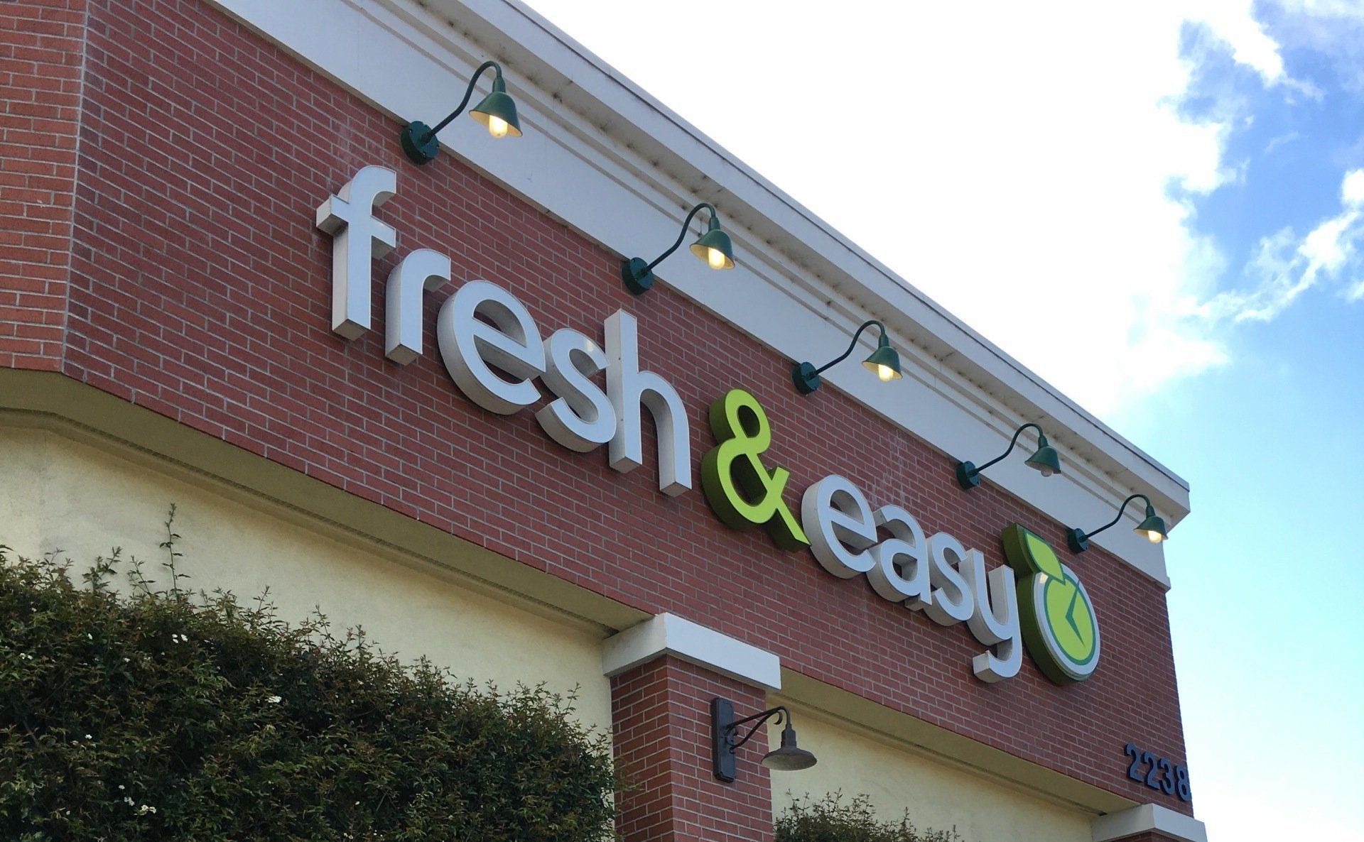 Fresh & Easy store sign on a brick building under string lights and blue sky