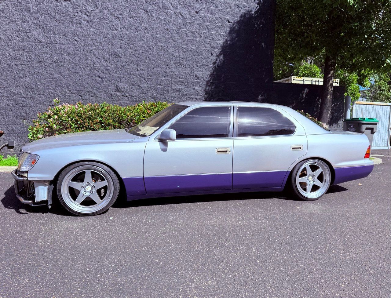 Lowered silver and purple coupe parked beside a wall in bright daylight