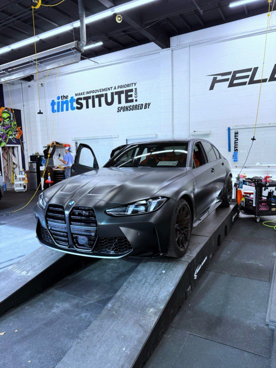 Matte gray BMW on a shop ramp inside a tinting/detailing garage