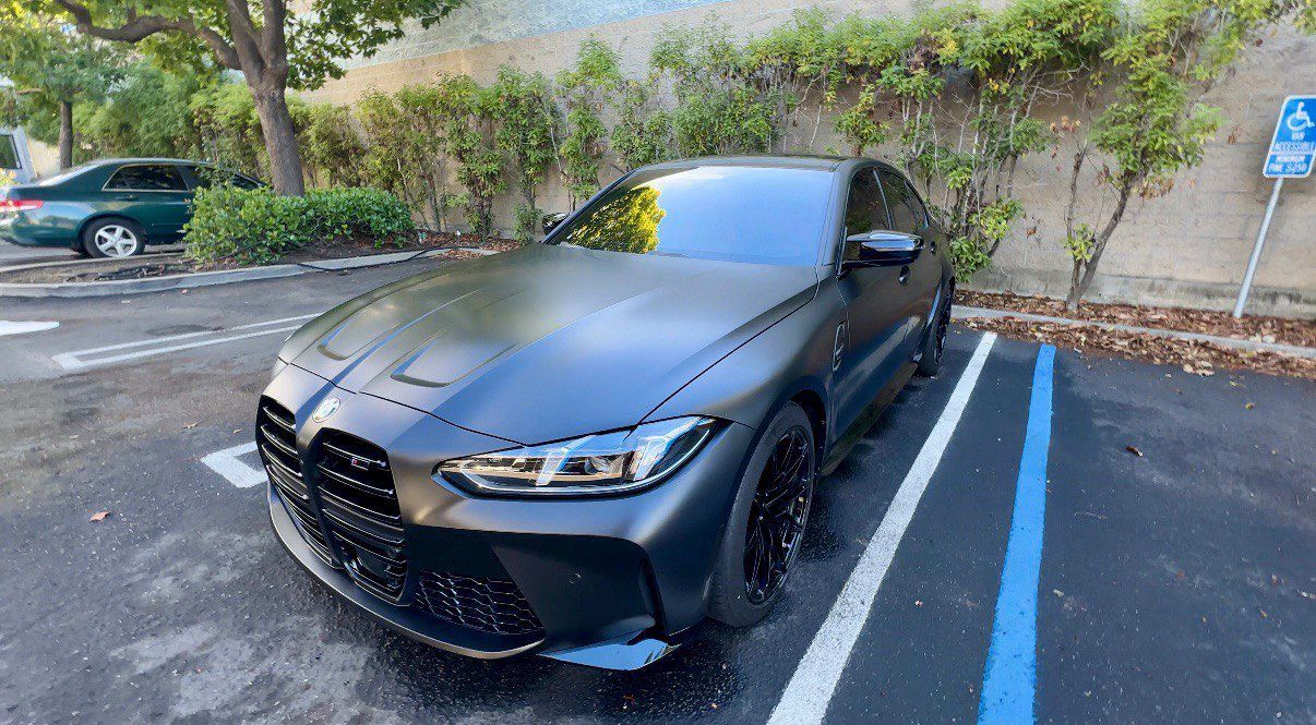Black sports coupe parked in a lot, front-left view, with matte finish and blue-striped accessible parking space lines