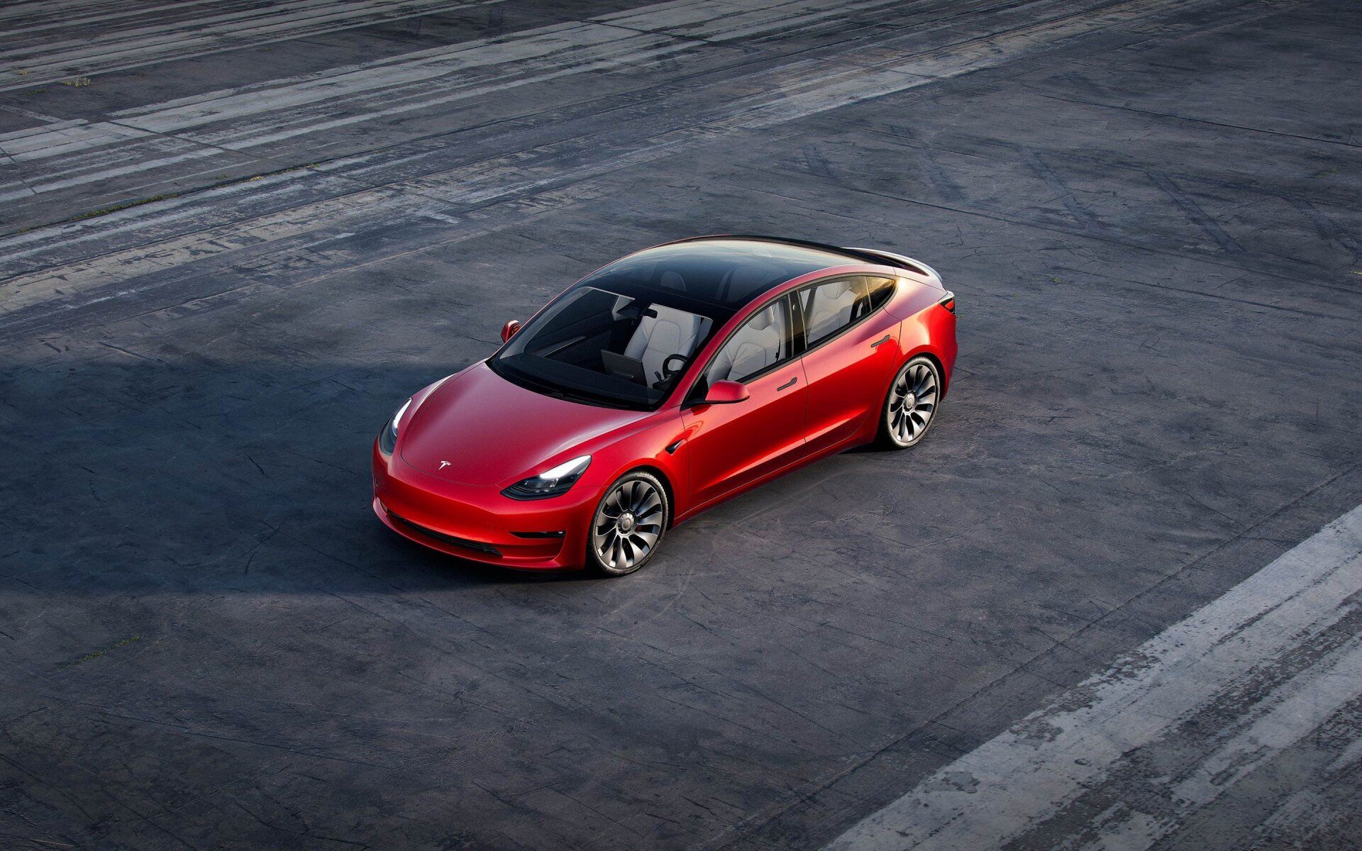 Red sports car driving on an empty paved road, viewed from above.