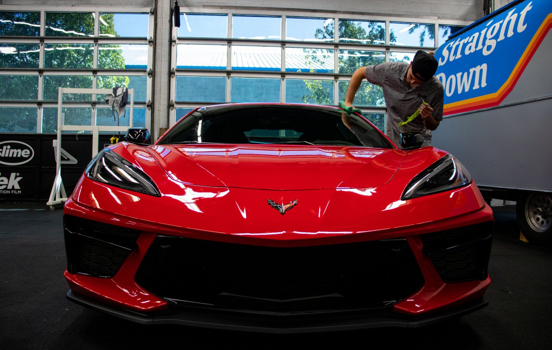 Red sports car on display indoors, with a person standing beside it in front of a glass wall.